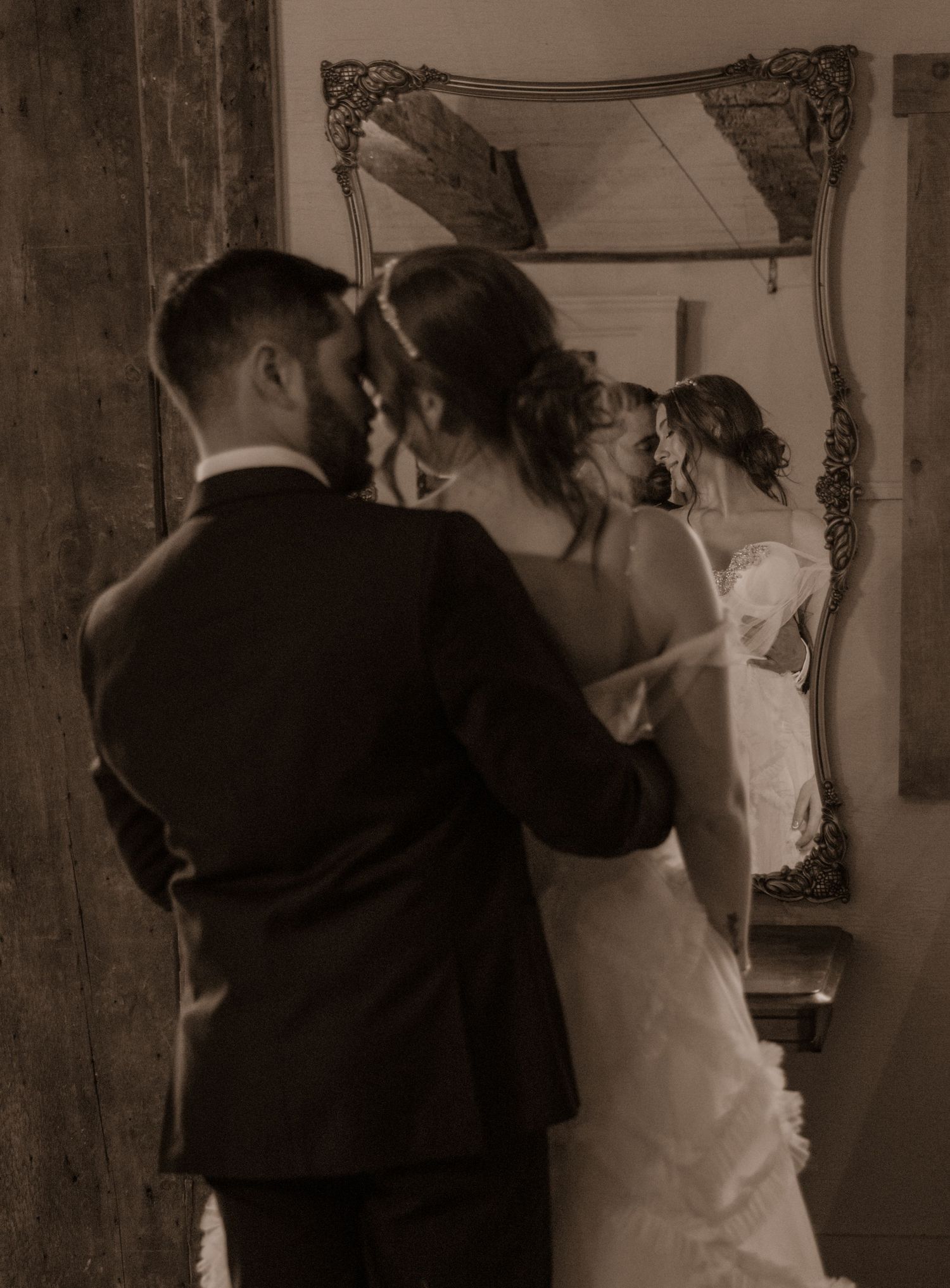 Vintage-style photograph of couple reflected in elegant mirror during wedding preparation.