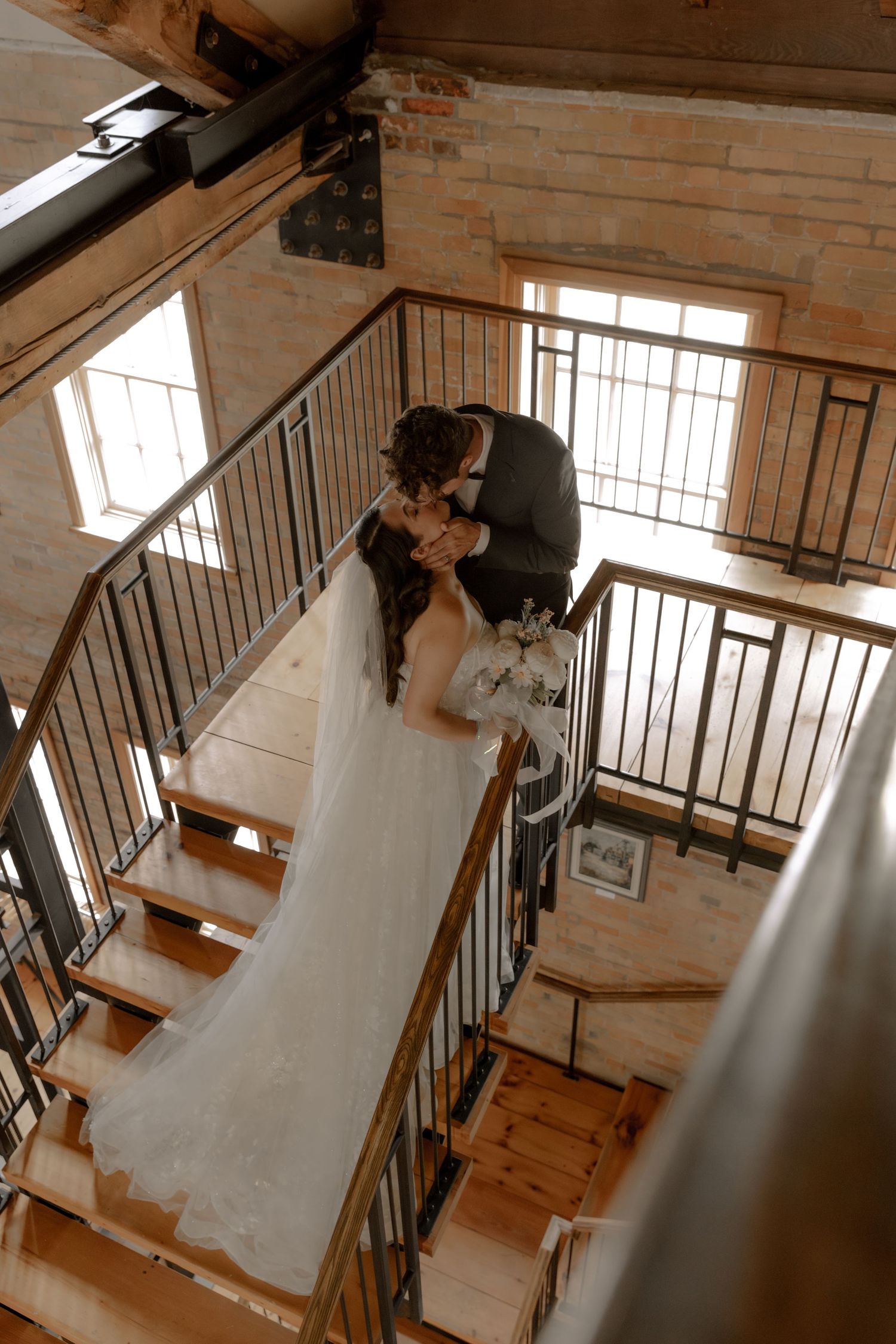 A couple at their wedding shares an intimate moment on a rustic wooden staircase with metal railings.