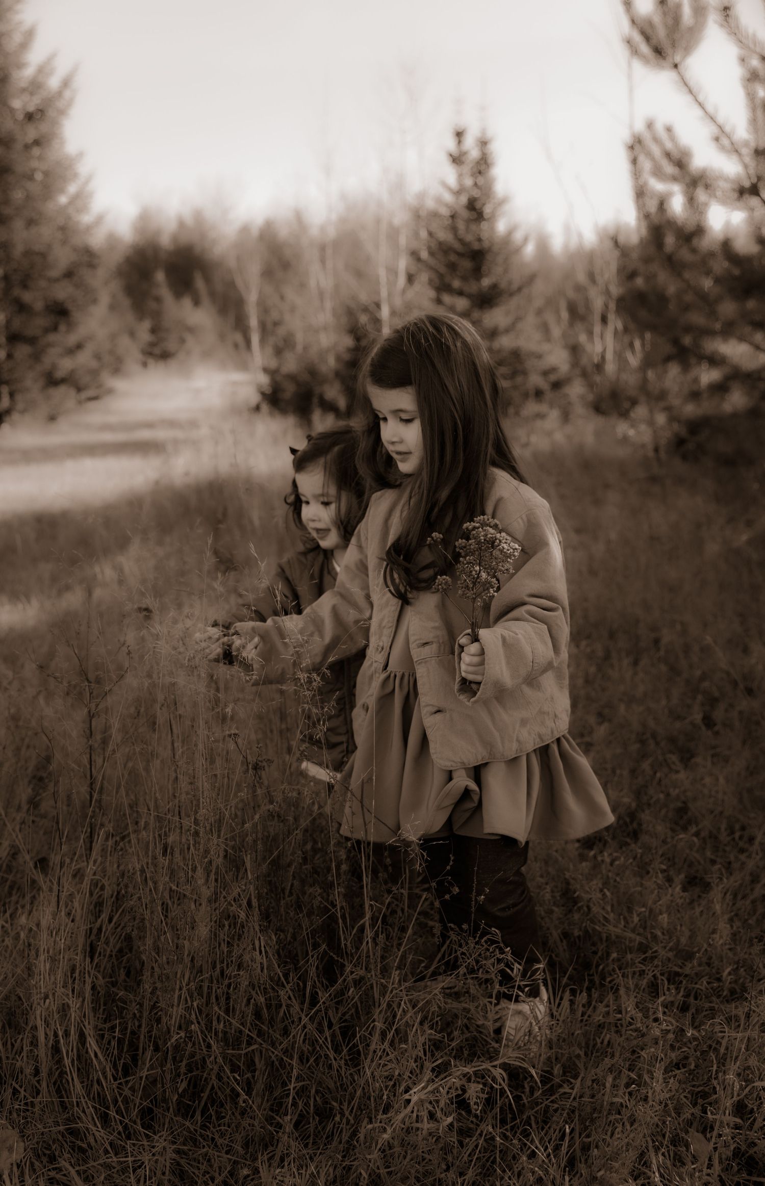 A sepia-toned photograph of two people exploring a field together on an autumn day.