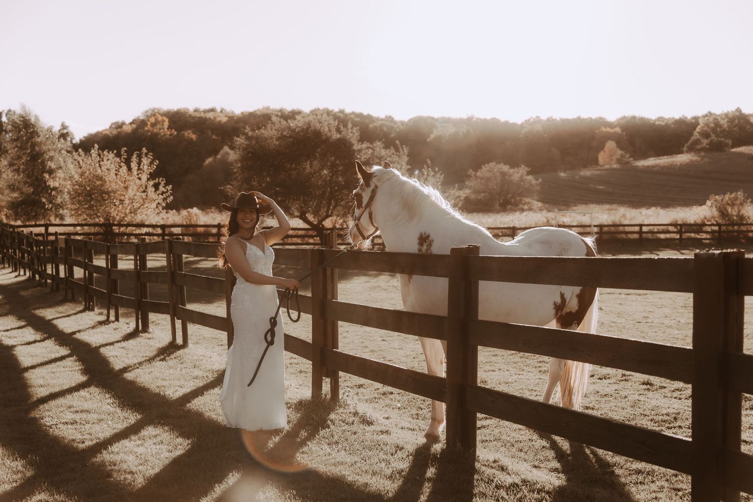 A white horse and wedding dress silhouette against a wooden fence during sunset.