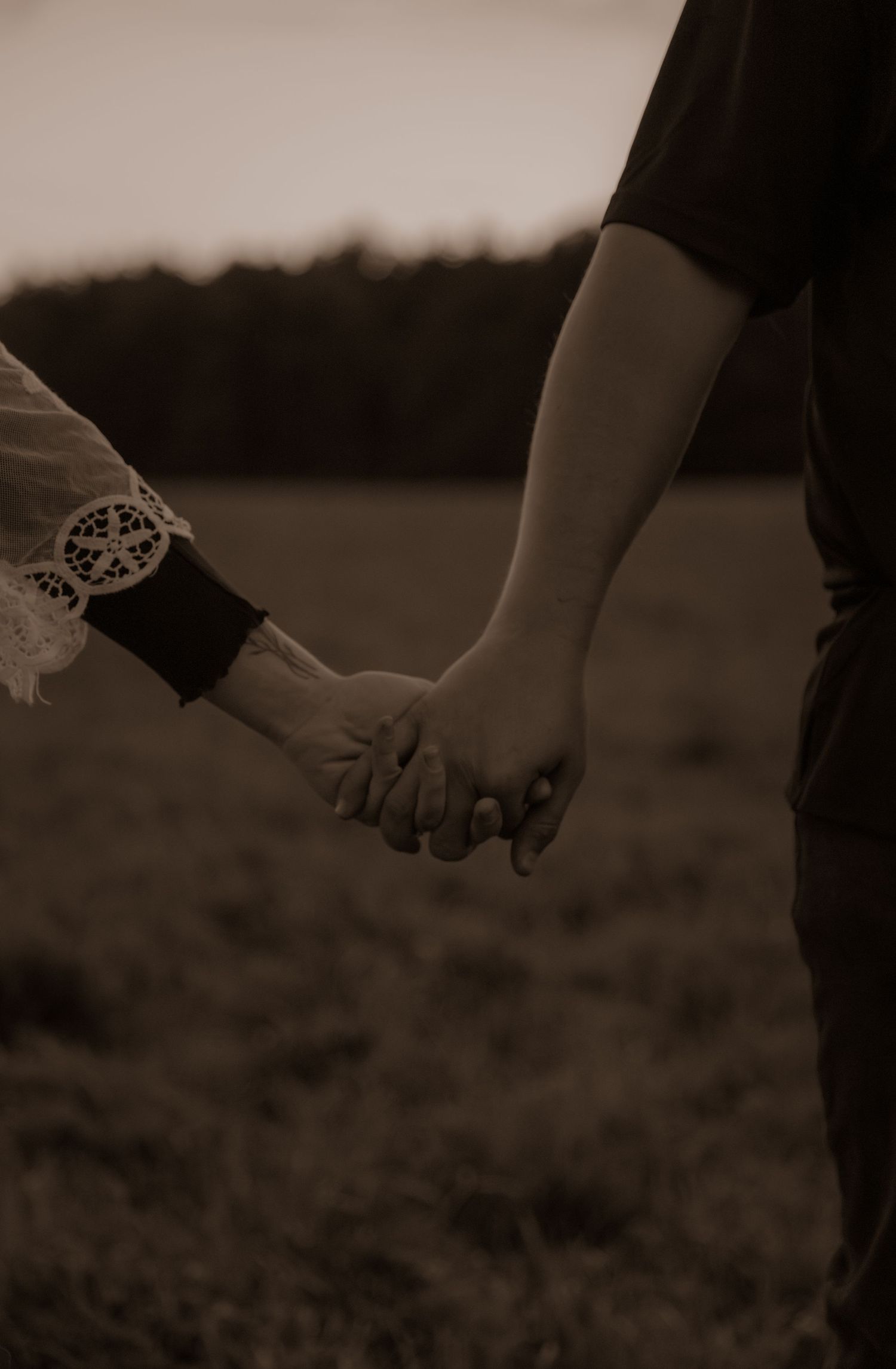 Romantic couple holding hands in sepia tones with lace sleeve detail.