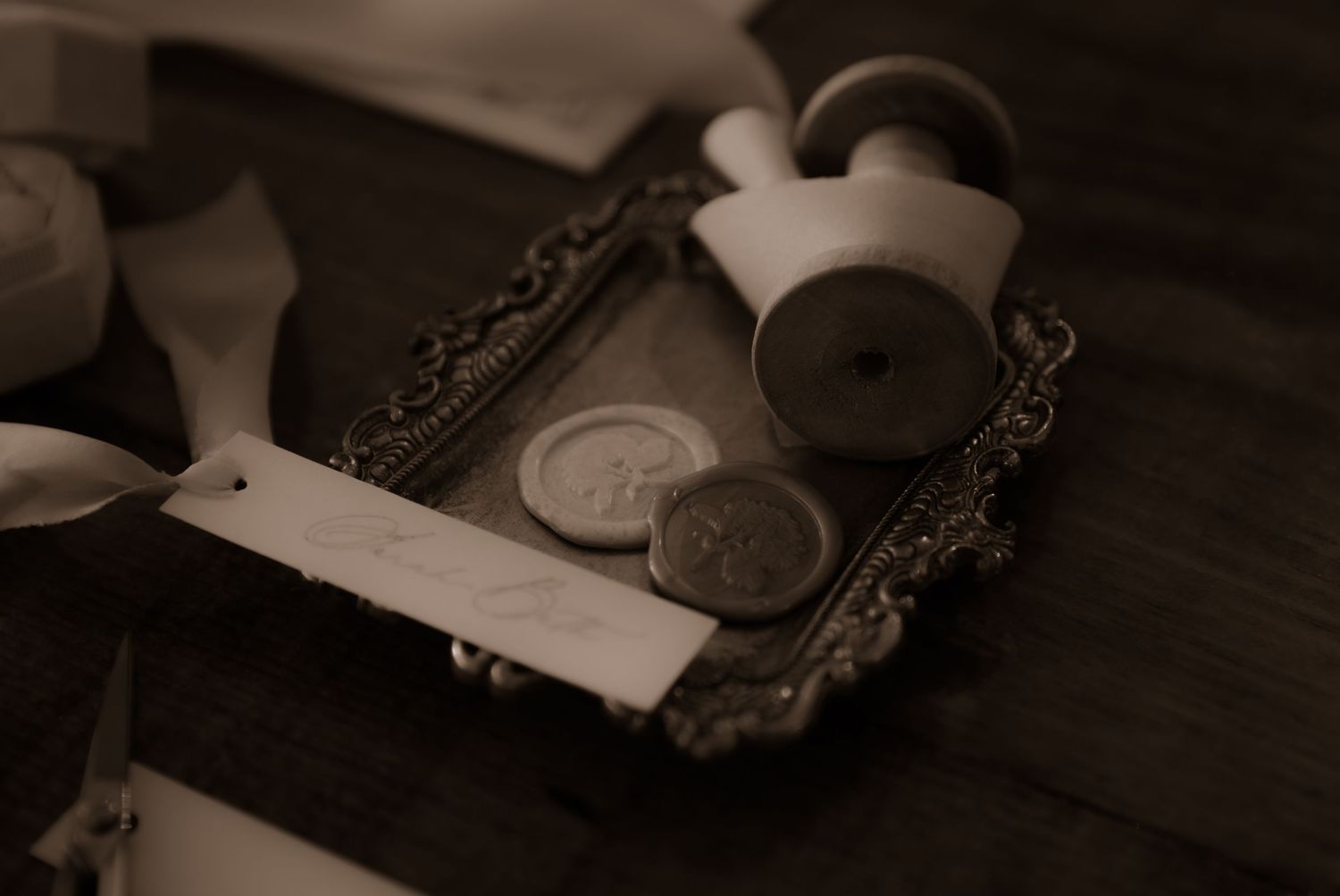 Wedding rings and decorative items arranged on a dark wooden tray in sepia tones.