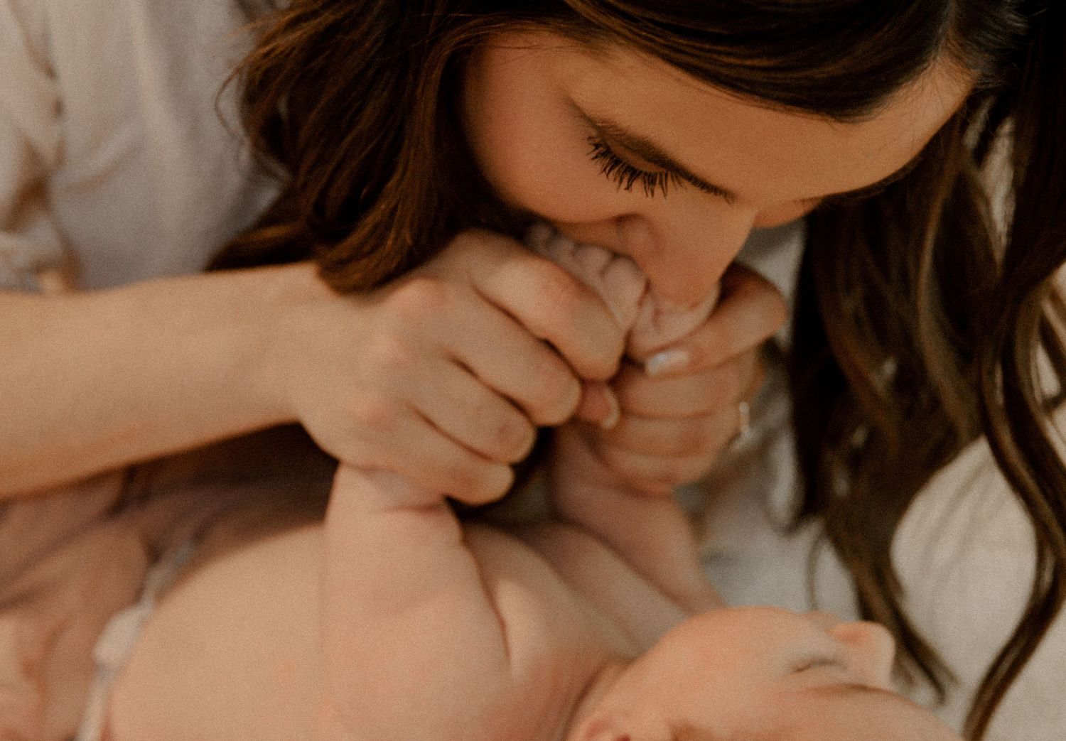 Parent giving tender loving kisses to baby's hand and foot in warm natural lighting.