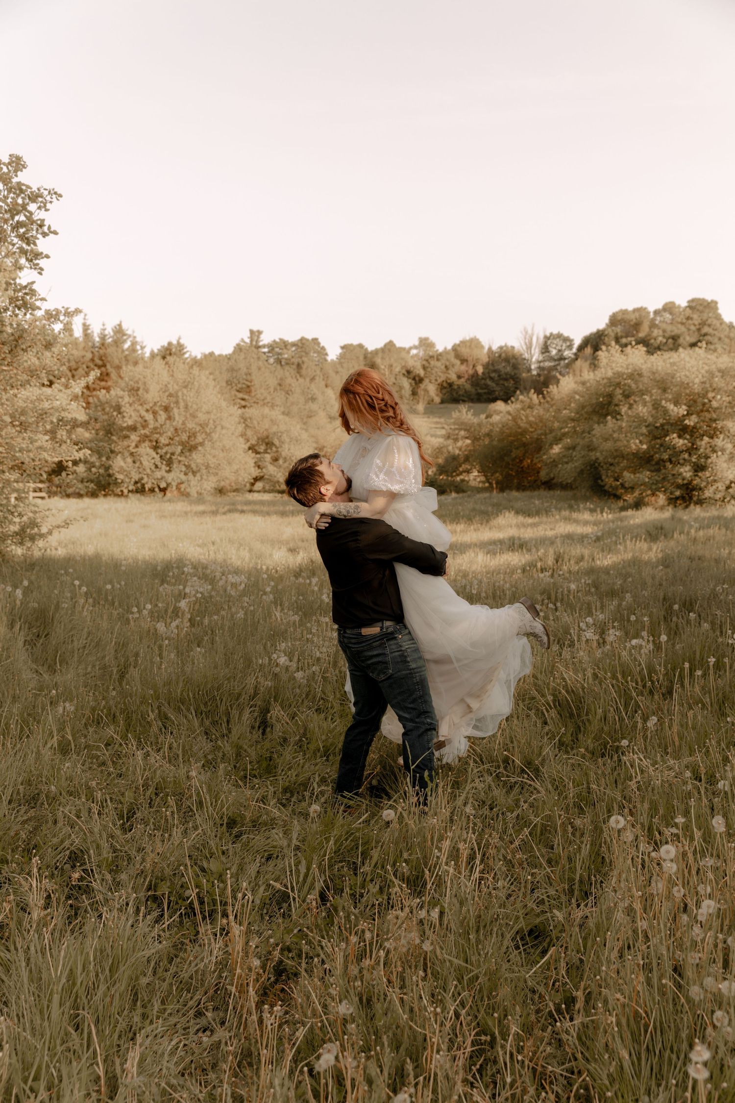Couple dancing and spinning in a sunlit meadow during their wedding photoshoot.