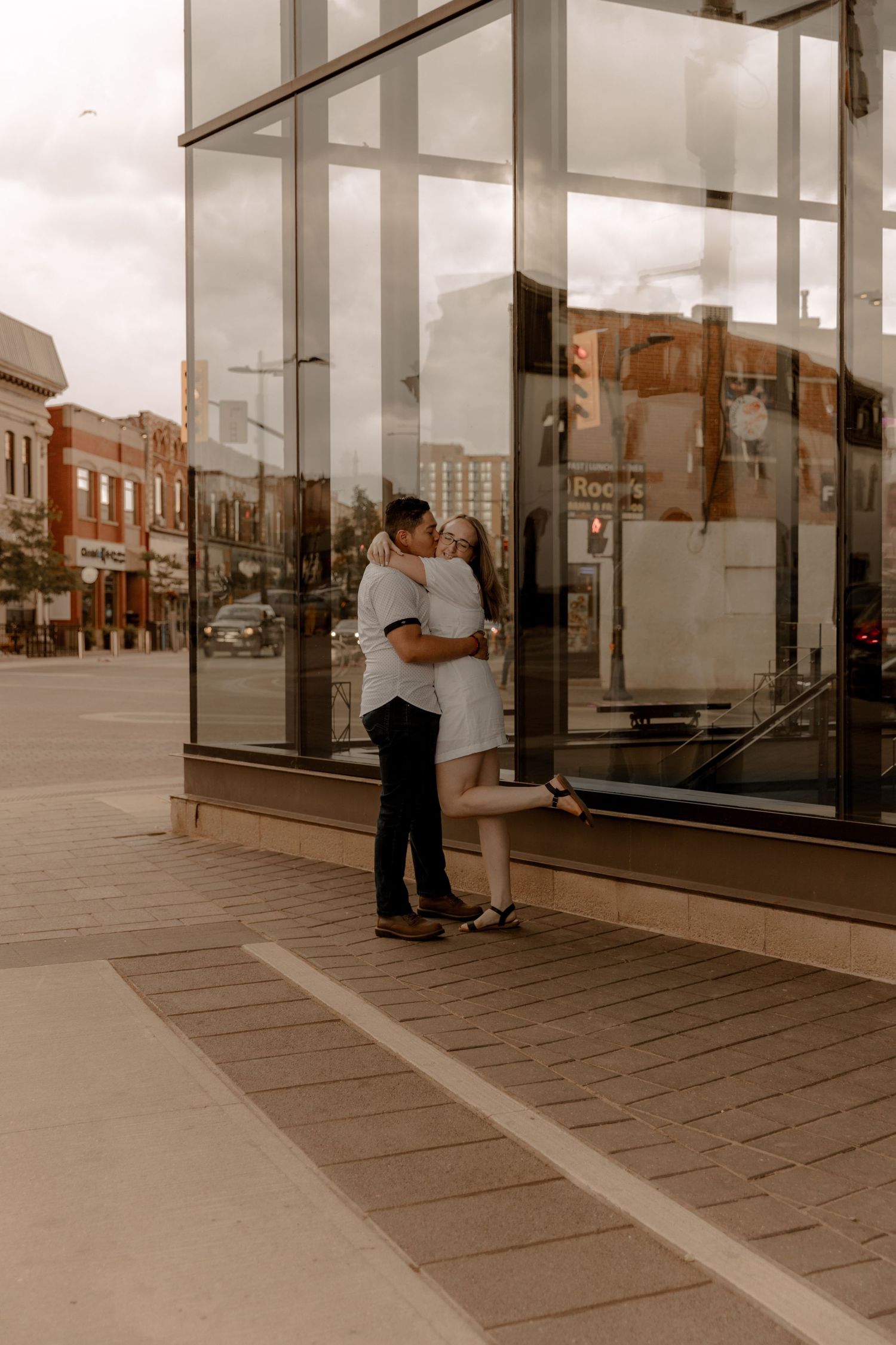 Two people sharing an intimate moment together against a glass storefront in a small town commercial district.