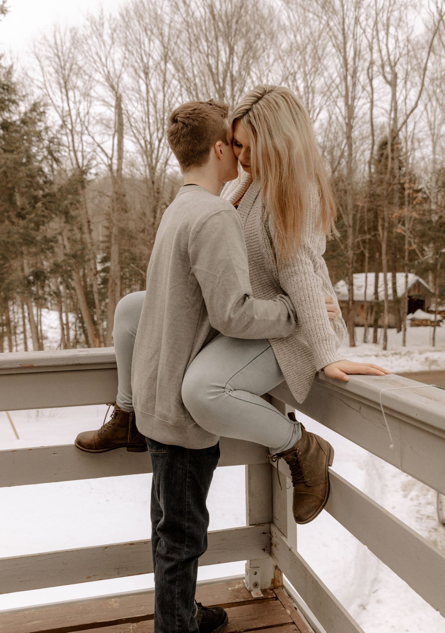 A couple sharing an intimate moment on a snowy bridge deck while wearing cozy winter sweaters.