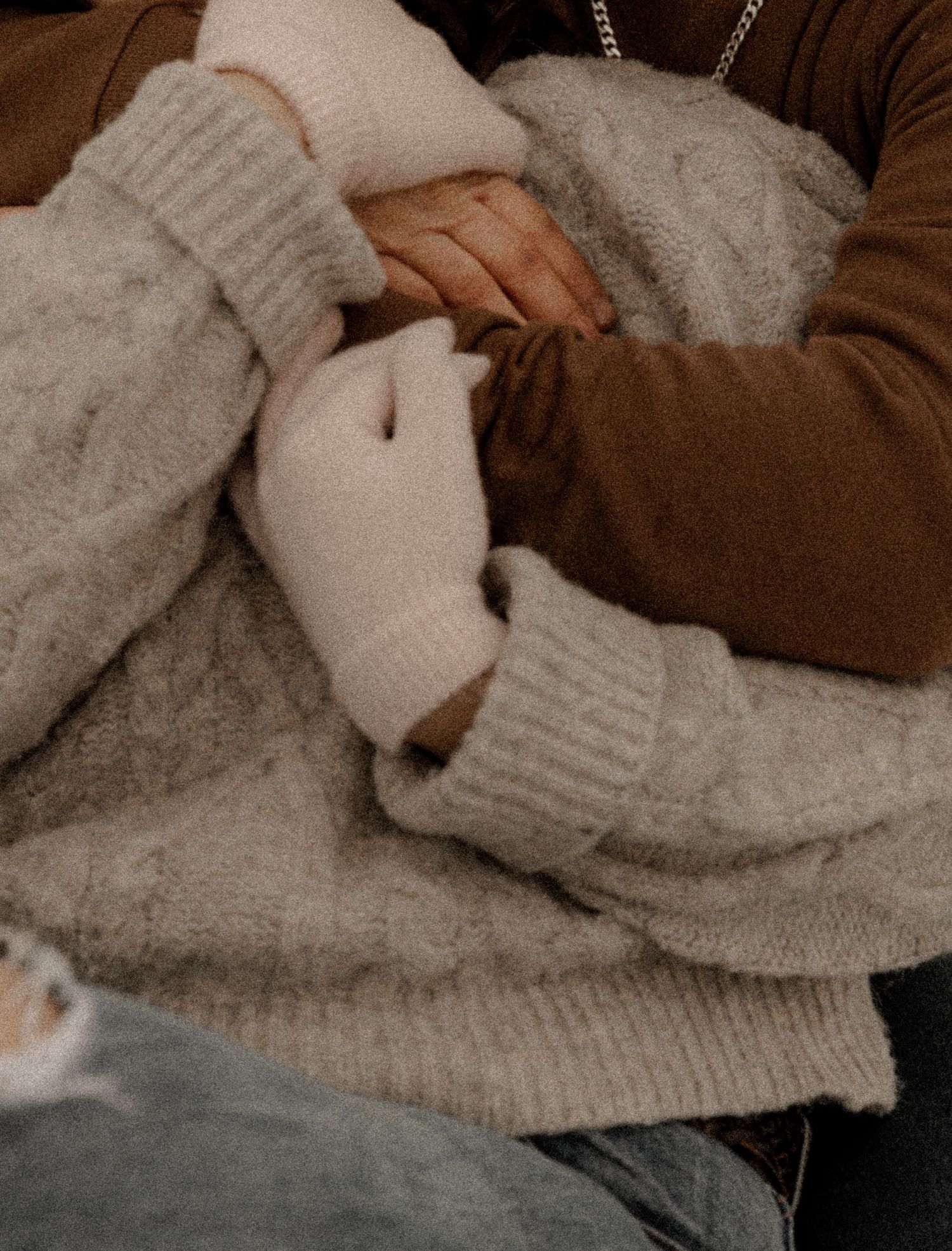 Two hands gently holding each other while wearing cozy knit sweaters in warm brown and beige tones.
