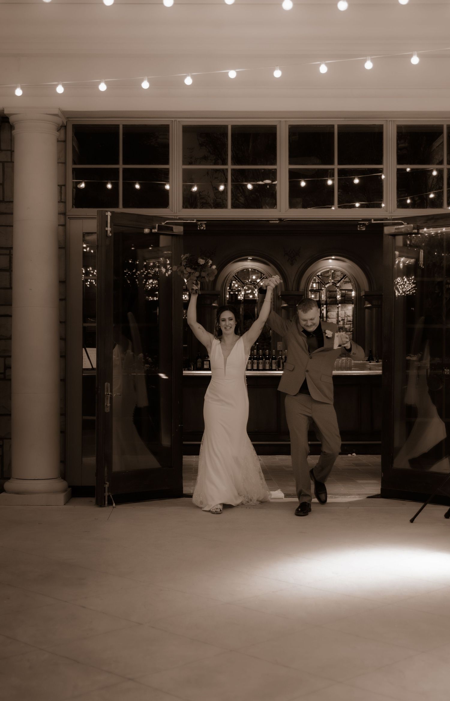Newlyweds dancing with joyful energy at their wedding reception under string lights.