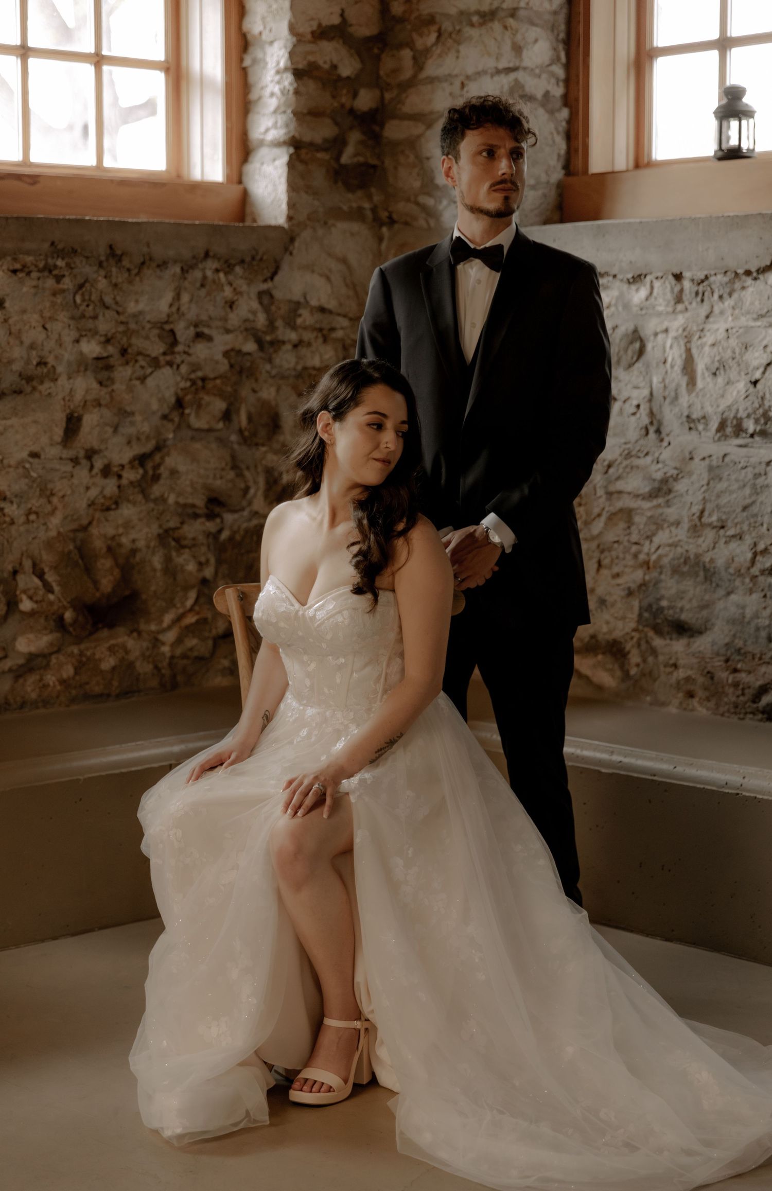 Wedding couple posing in a rustic stone room with natural window lighting.
