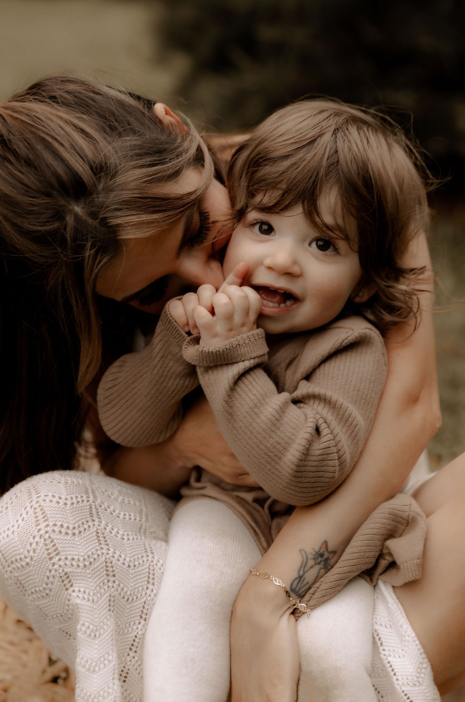 A tender moment captured between parent and child wearing a brown sweater against a dark background.