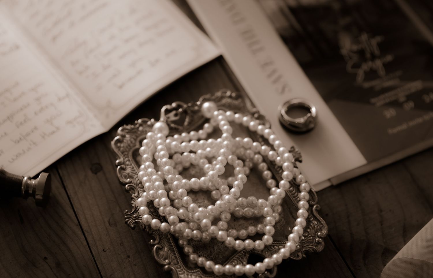 Pearl necklace and rings arranged on vintage book pages in sepia tones.
