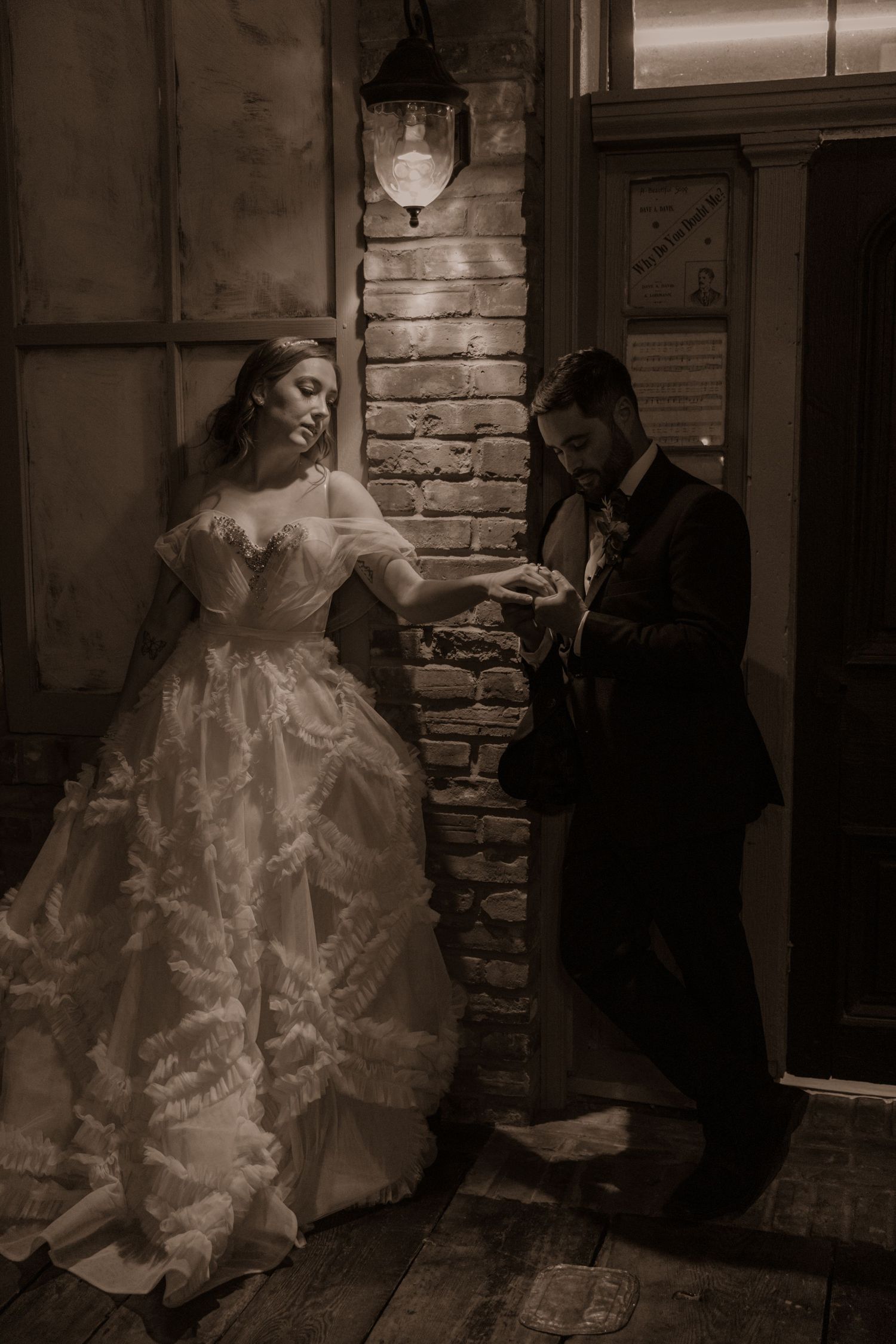 Vintage-style wedding photo with couple sharing intimate moment by brick wall and antique door.