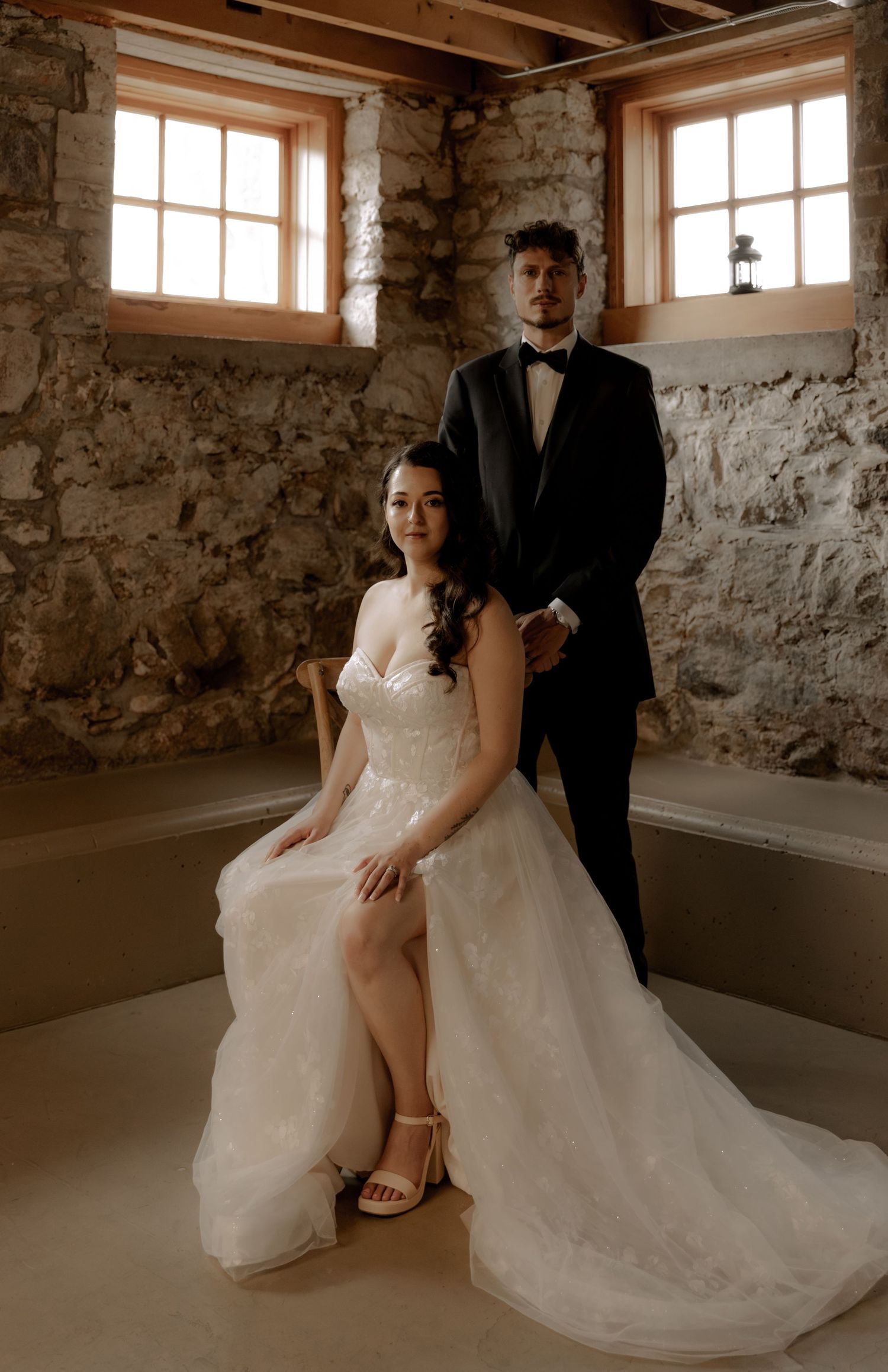 Wedding portrait in rustic stone room with natural window light and exposed wooden beams.