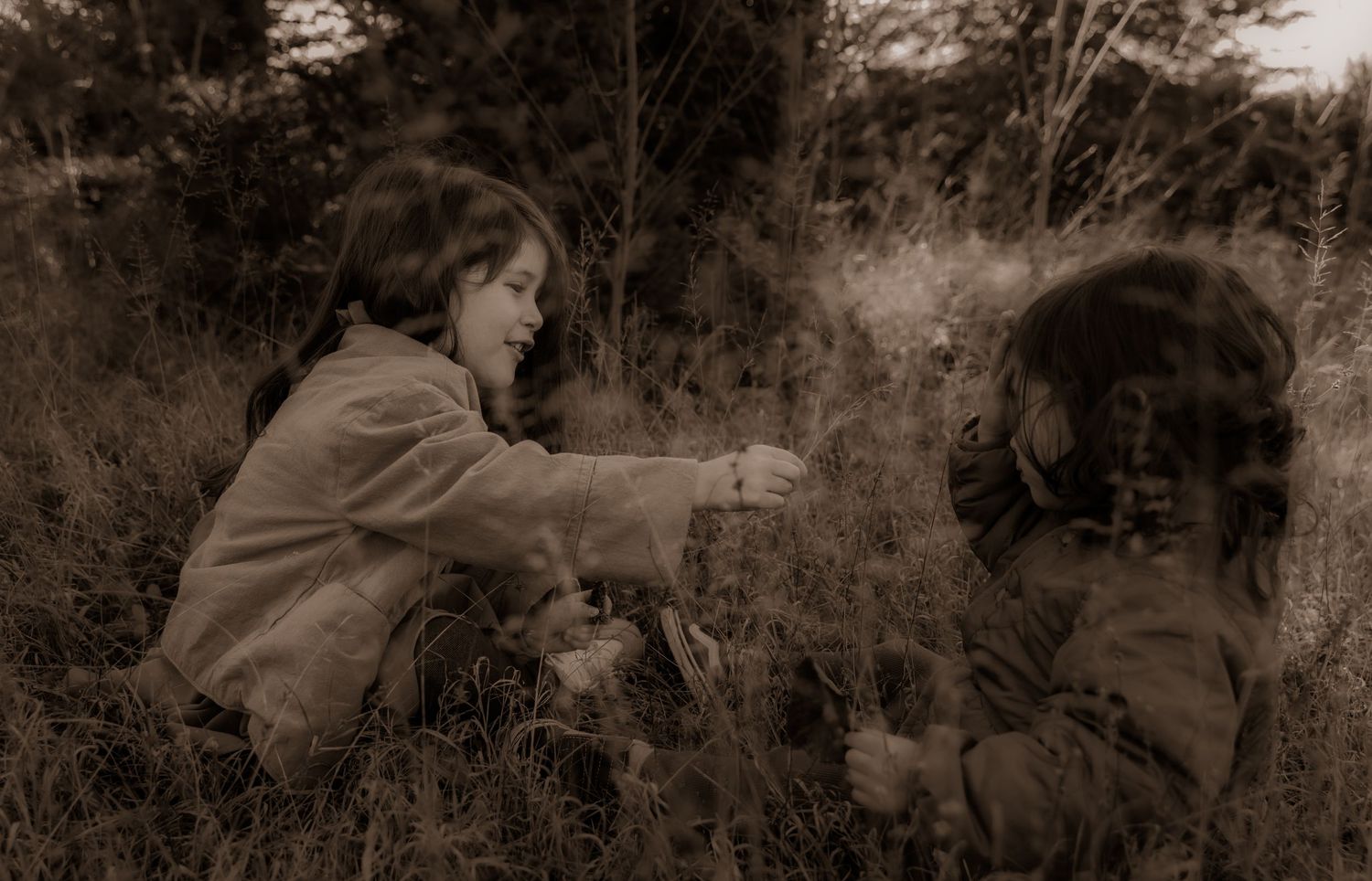 Two young children play together outdoors in a sepia-toned vintage photograph showing playful interaction.