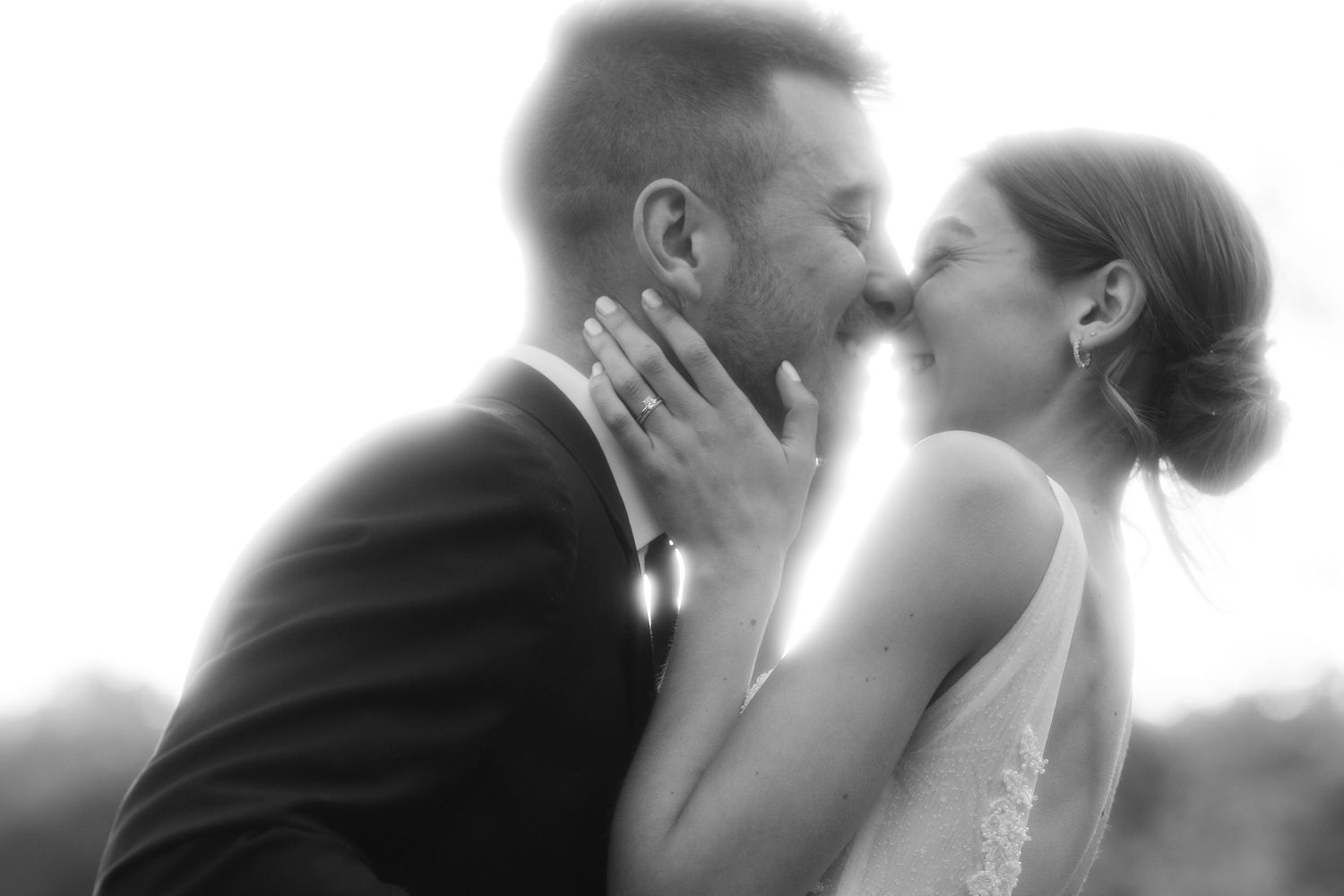 A romantic black and white wedding photo capturing two people sharing a tender kiss in soft focus.