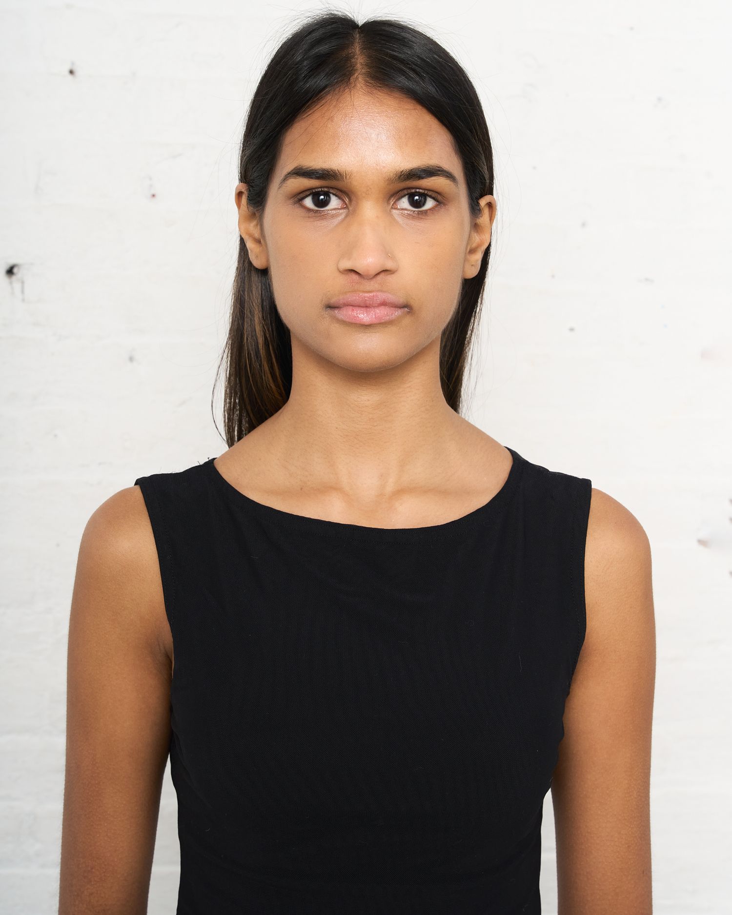 Studio headshot of model wearing black sleeveless top against white wall. Modeling Digitals
