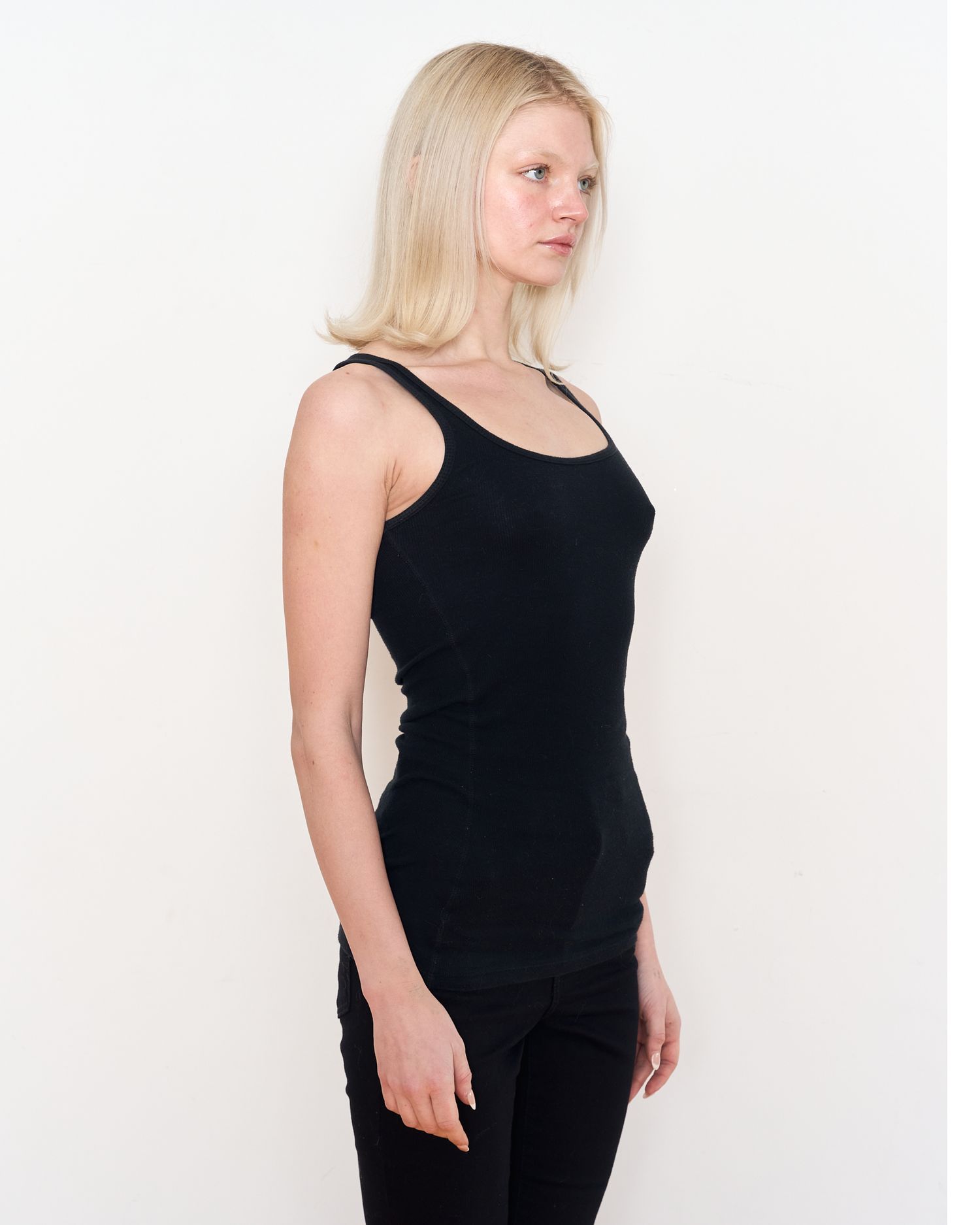 Side view of model wearing black sleeveless top against white background. Modeling Digitals