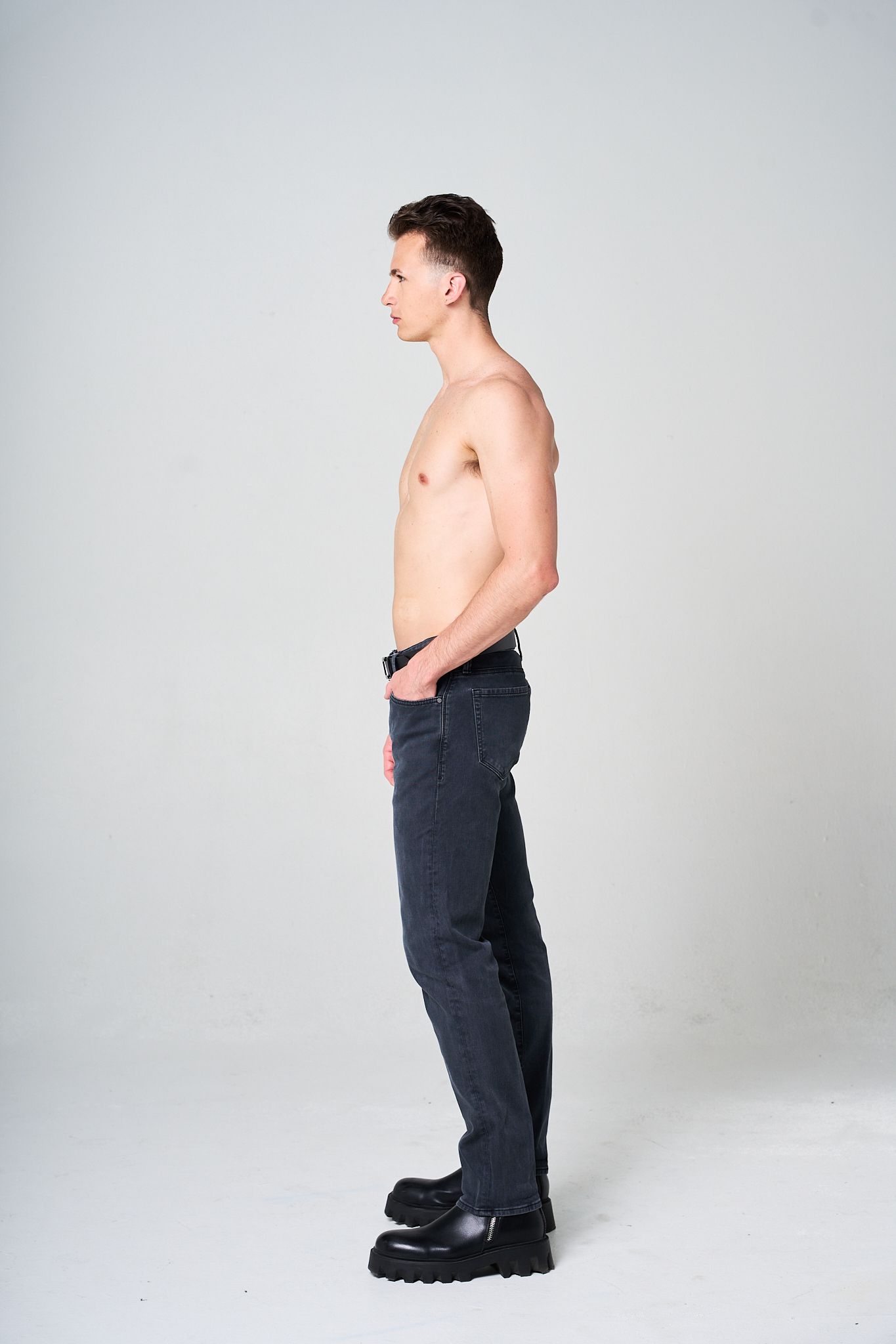 Side view of model in dark jeans against light grey studio background. Modeling Digitals