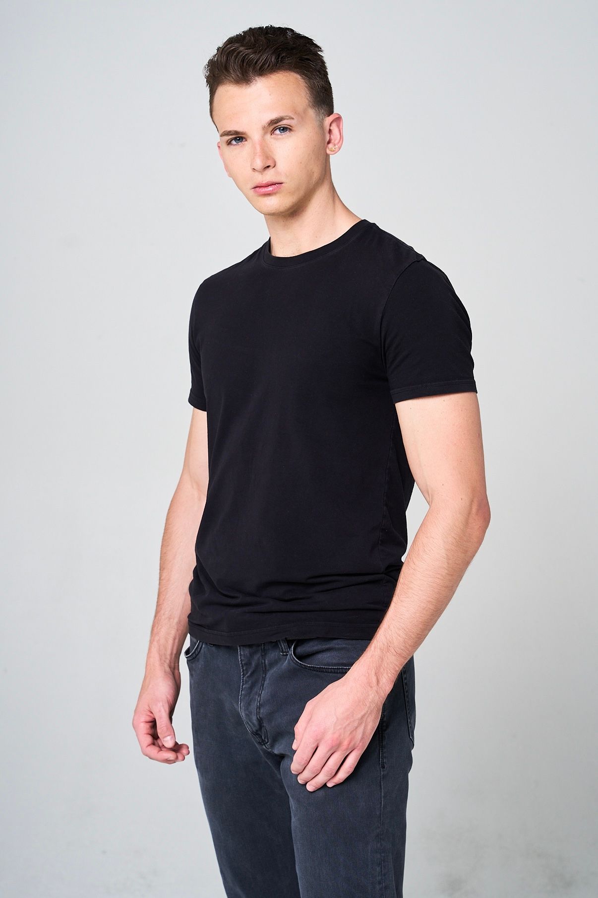 Fashion model poses in black t-shirt and jeans against neutral studio backdrop. Modeling Digitals