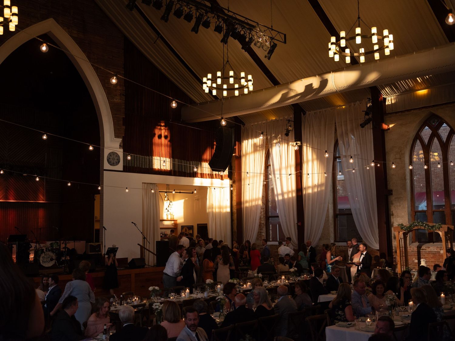 Elegant wedding reception venue with warm lighting and circular tables set up beneath decorative chandeliers.