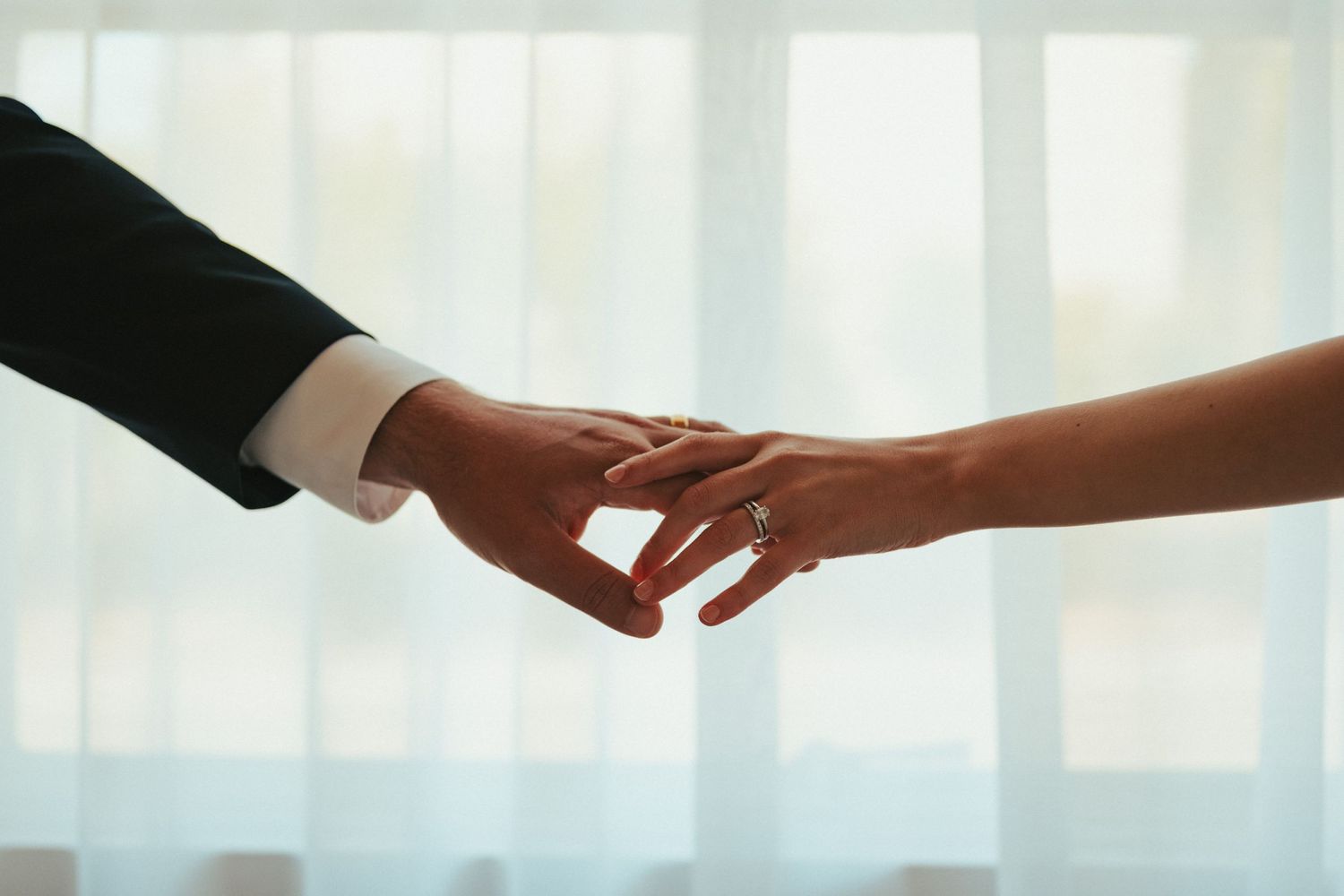 Two hands reaching toward each other against a bright window background.