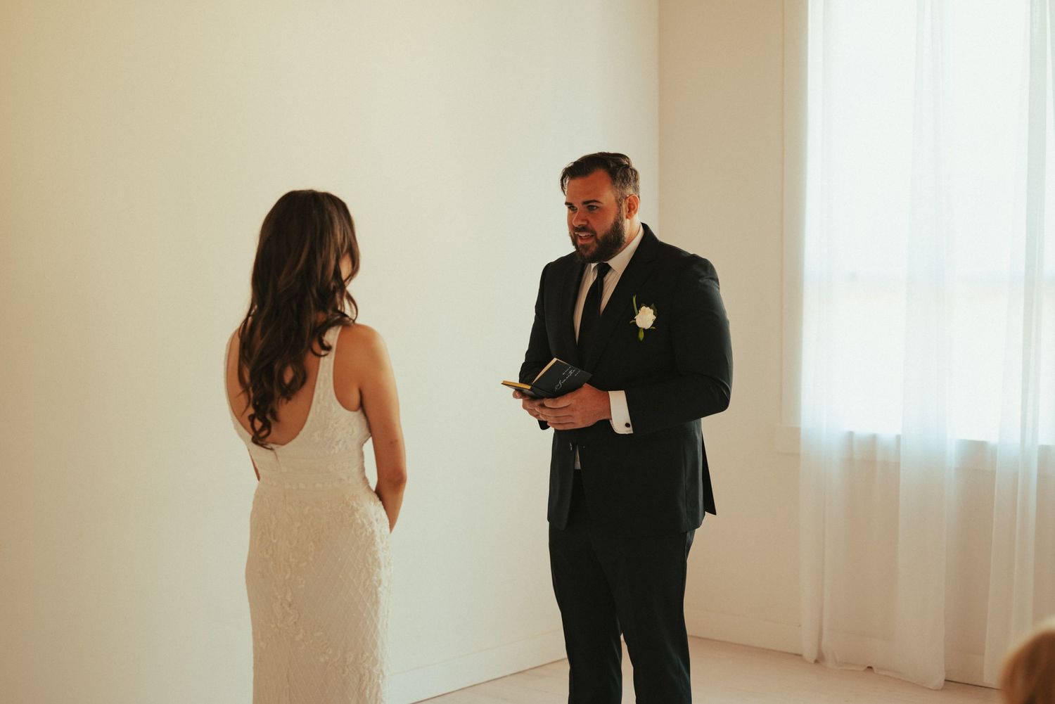 A couple exchanges private vows while standing in a minimalist white room.