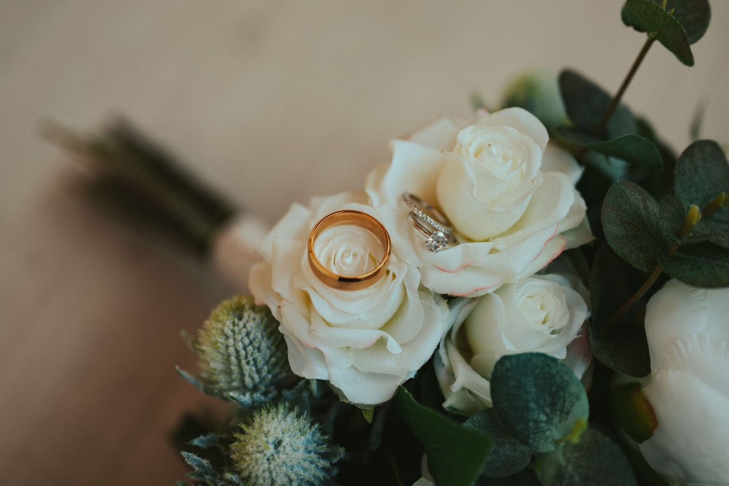 Wedding rings nestled among white roses and green foliage in a beautiful floral arrangement.