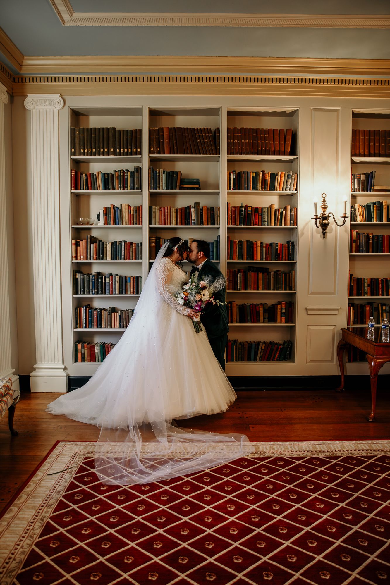 Elegant library venue with wall-to-wall bookshelves and ornate rug showcasing wedding moments.