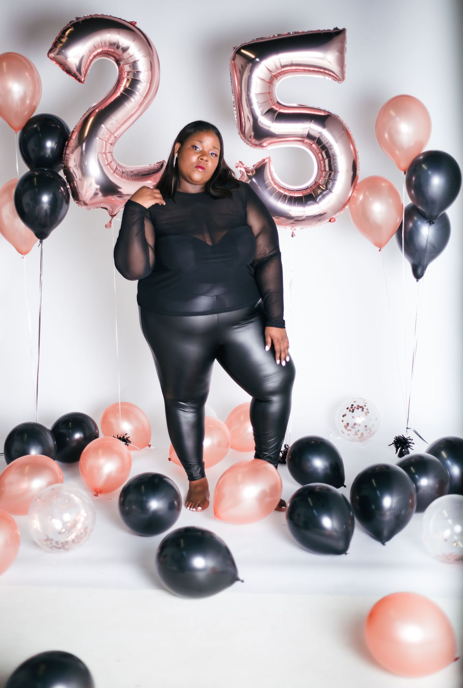 Festive photo shoot setup with rose gold and black balloons against white backdrop.