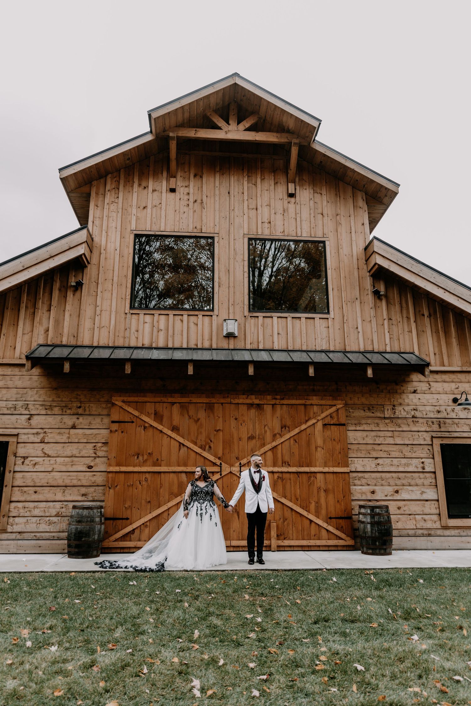 Couple posing in front of rustic wooden barn doors on their wedding day for symmetrical photo.