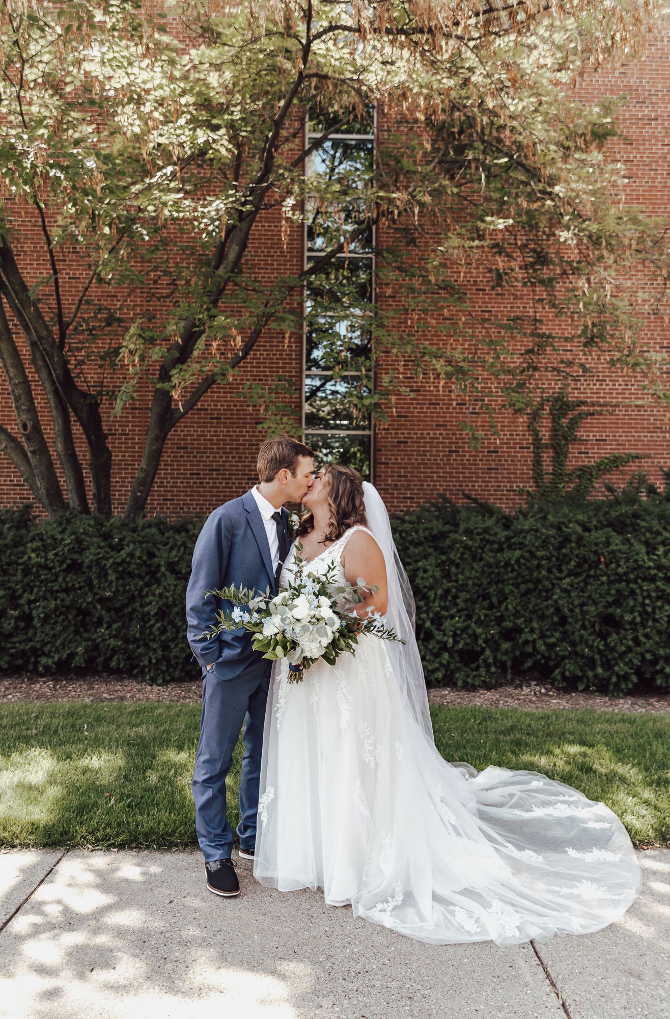 Springtime wedding portraits captured against blooming trees and brick building backdrop.