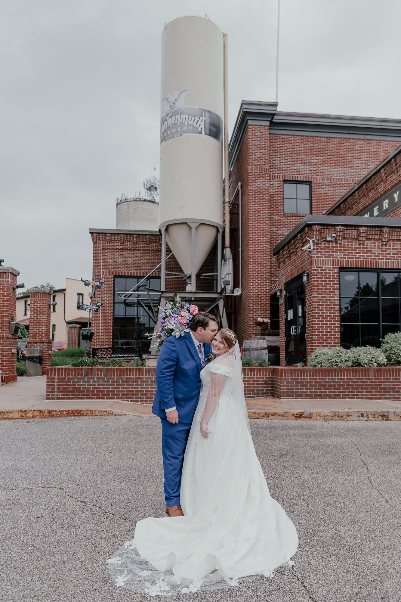 Wedding couple shares intimate moments outside industrial brick venue with classic styling.