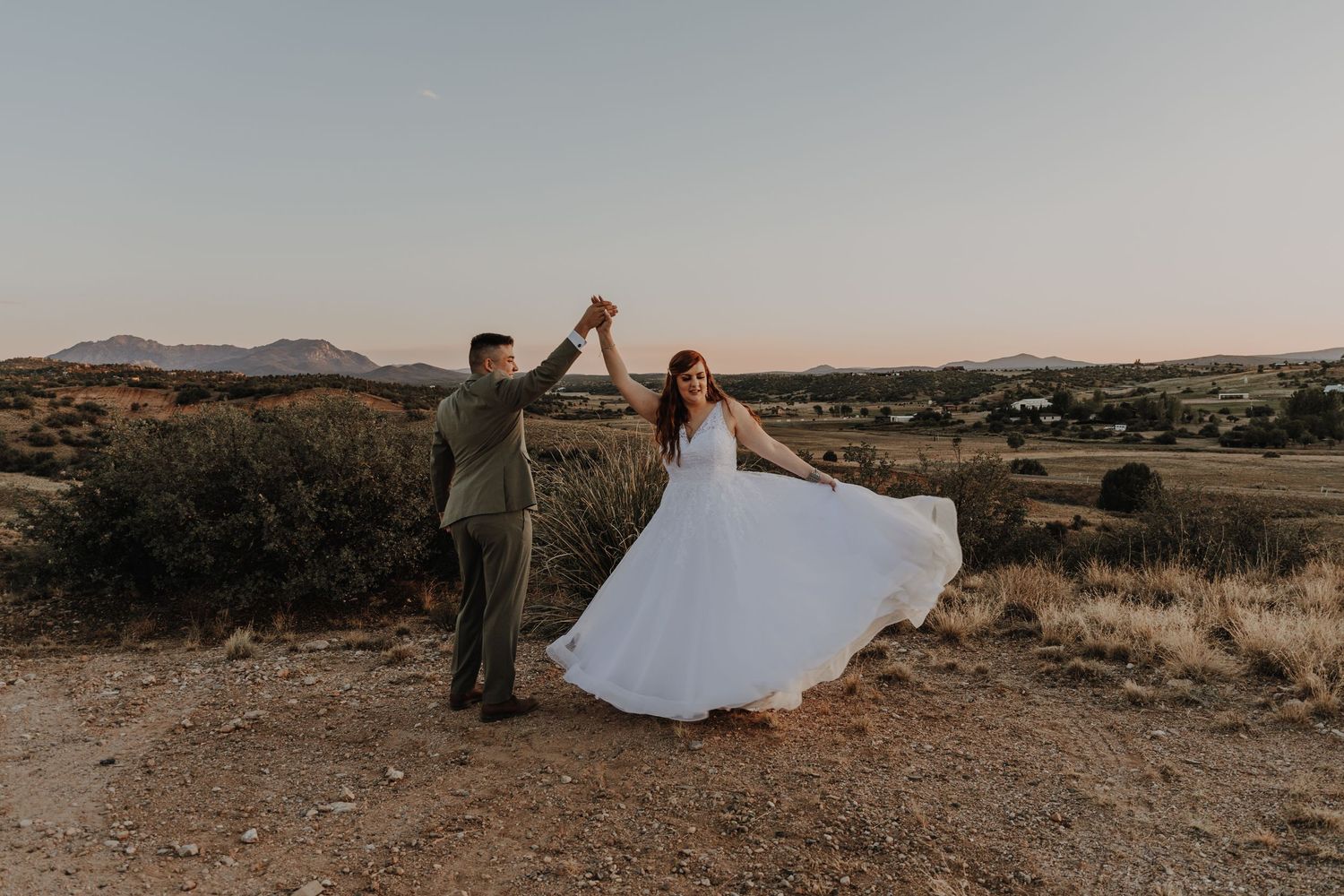 Wedding couple dancing and twirling on hilltop during sunset.