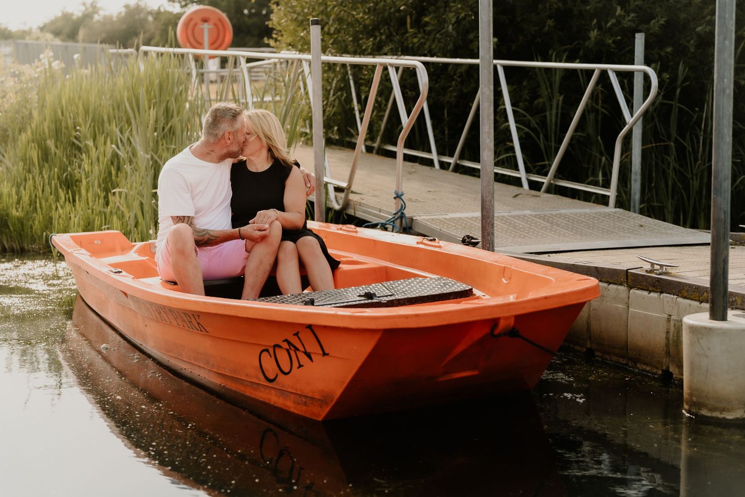 Couple sitting together in an orange boat on calm waters near a dock.