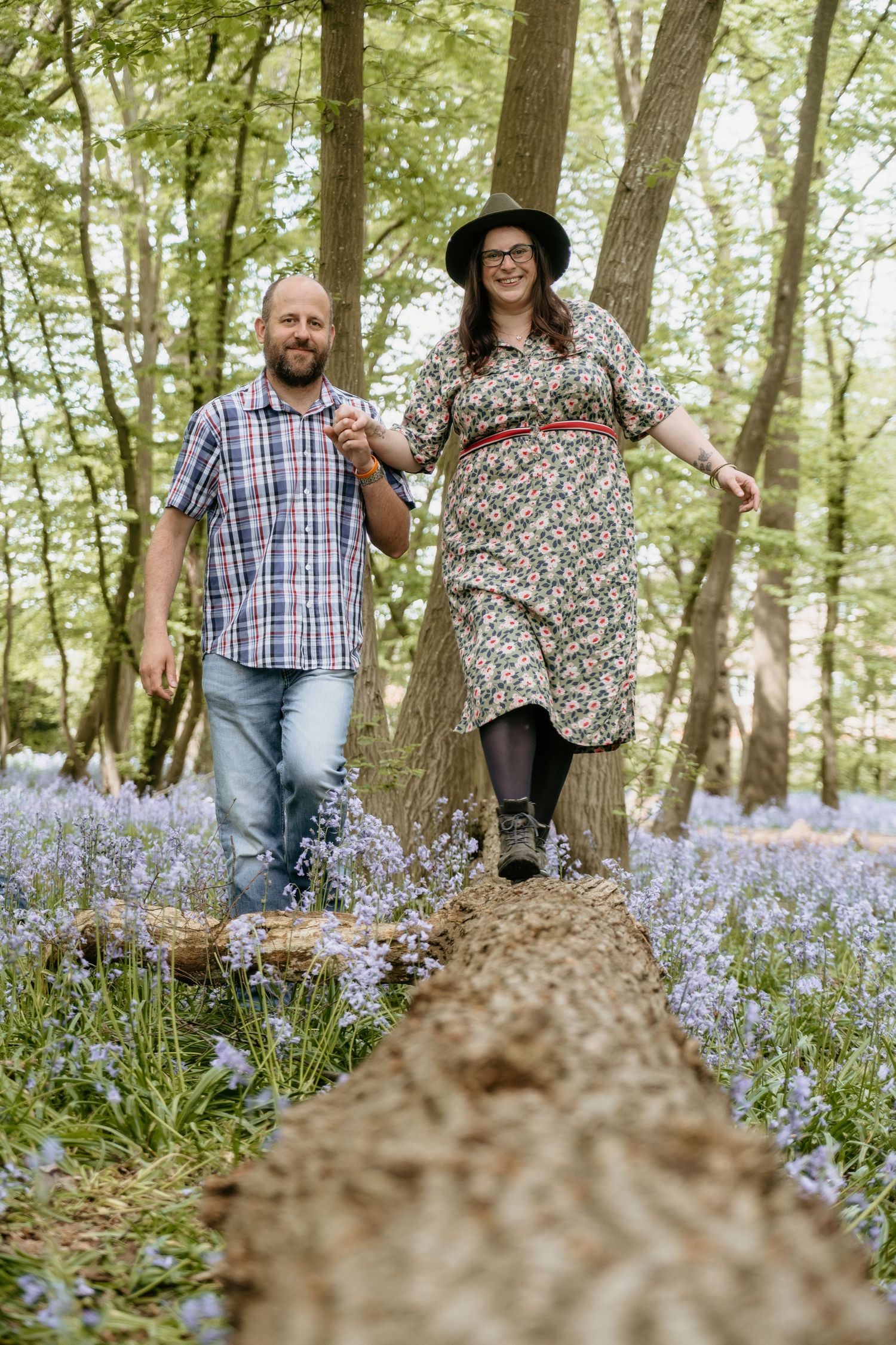 Couple walking together on a fallen tree trunk surrounded by blooming bluebells in a spring forest.