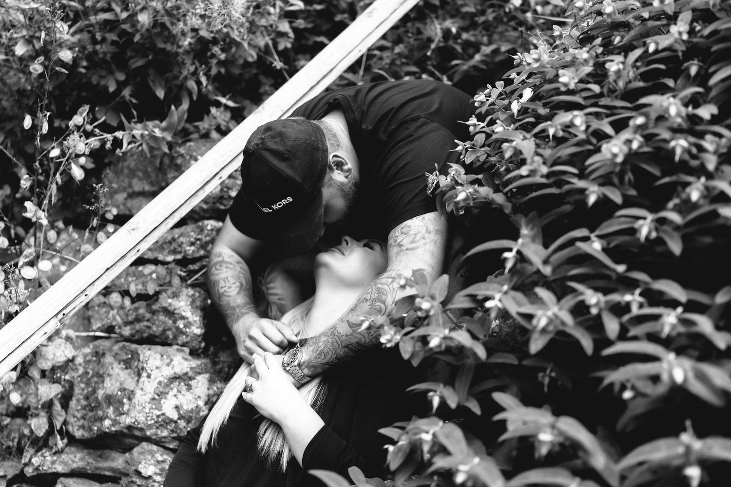An artistic black and white photo of a couple sharing an intimate moment on stone steps.