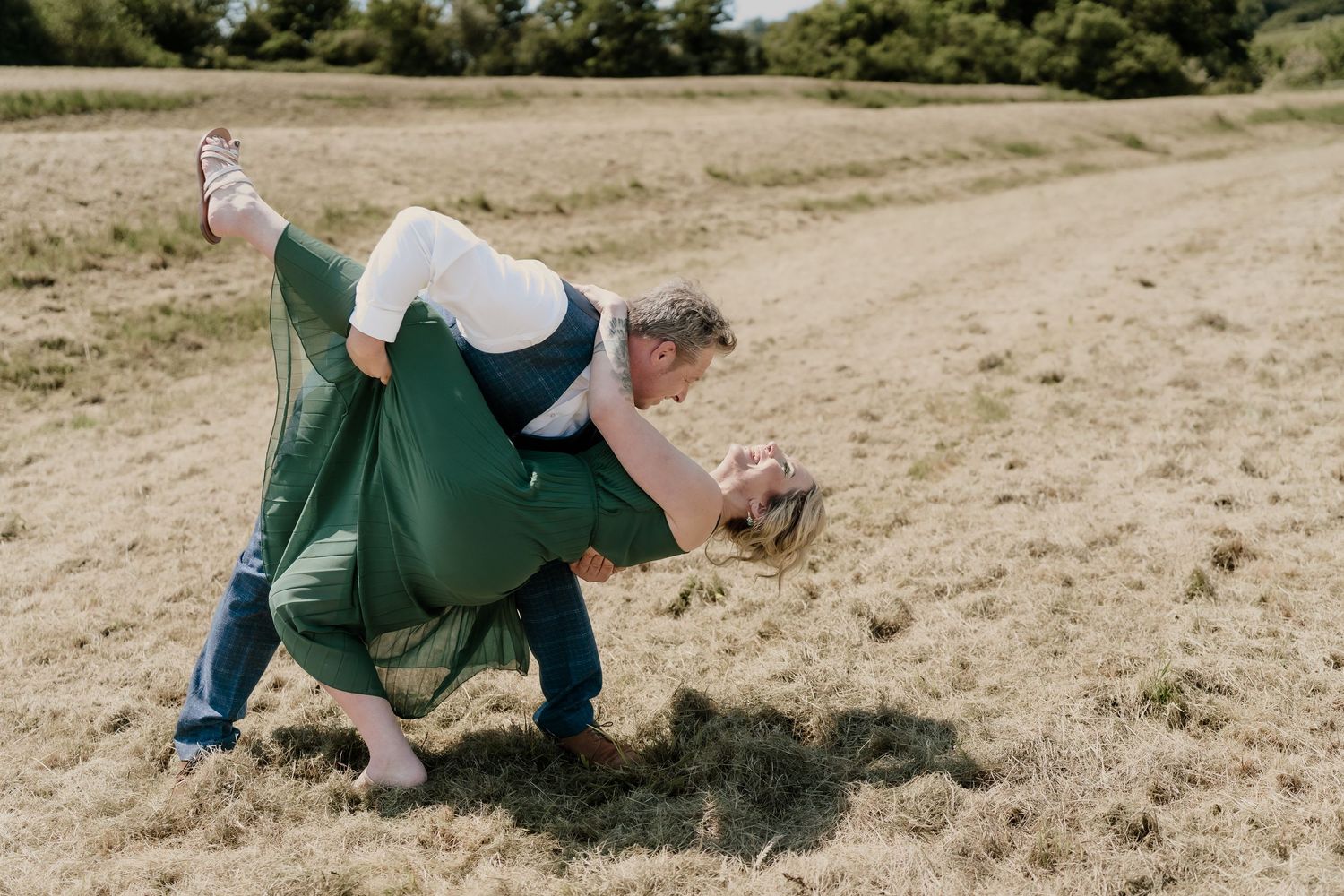 Playful couple rolling and laughing together in a grassy meadow.