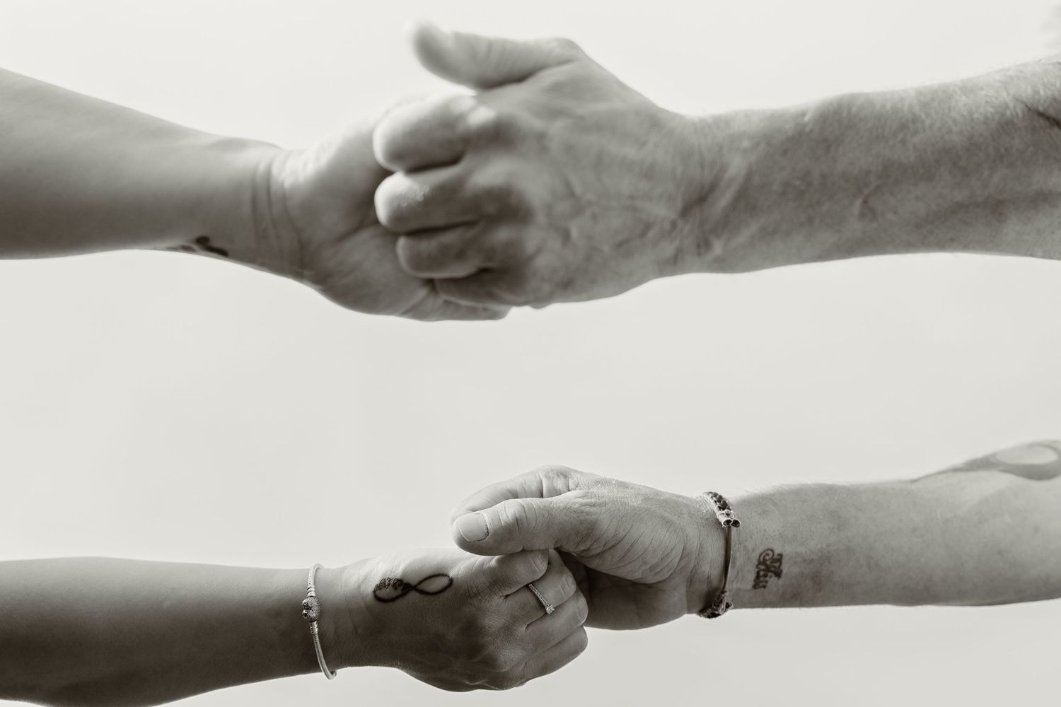 A black and white close-up of two hands reaching to hold each other symbolizing connection.