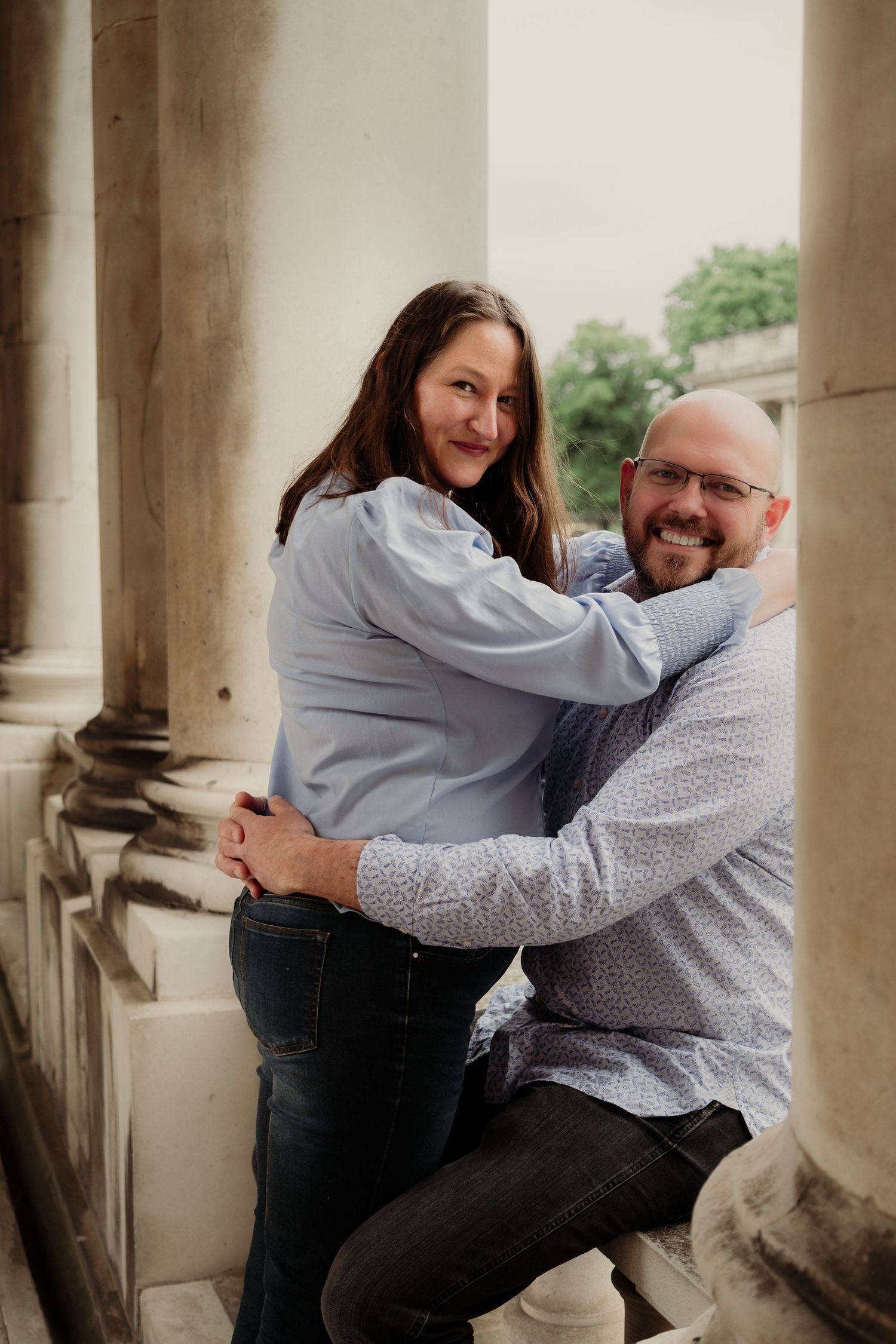 A playful engagement portrait of a couple posing between classical columns.
