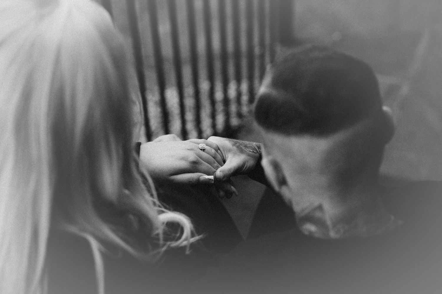 A black and white close-up of hands with engagement rings intertwined.