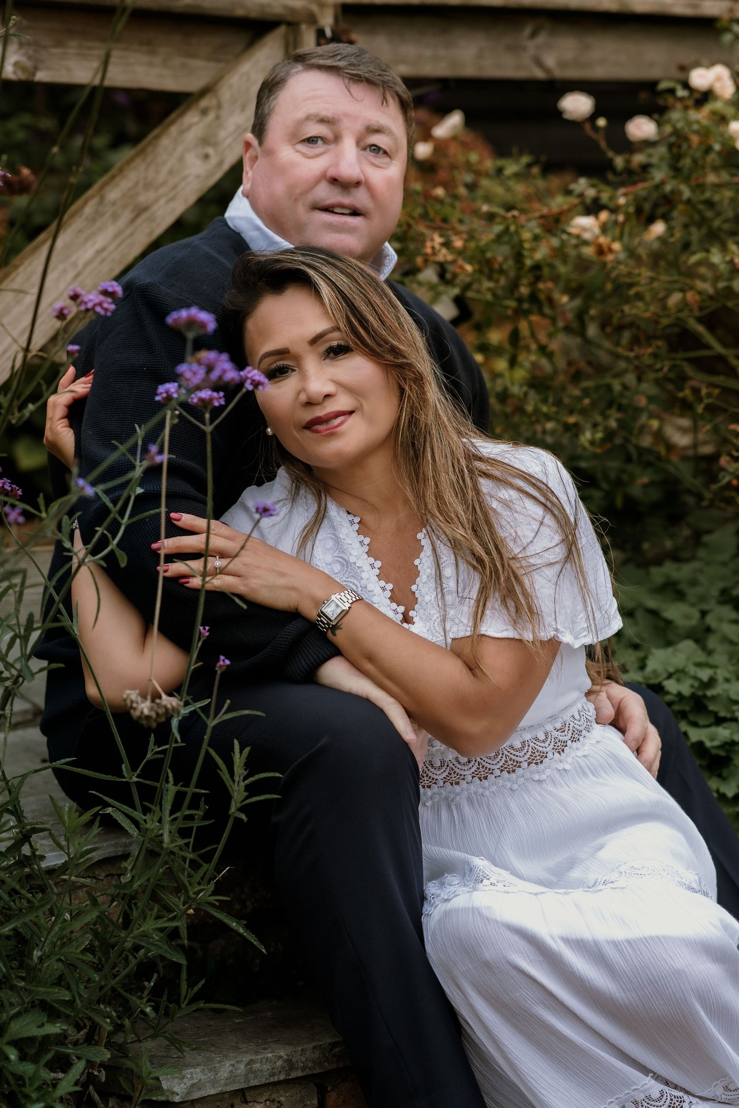 A romantic outdoor portrait of a couple in formal attire sitting among purple flowers.