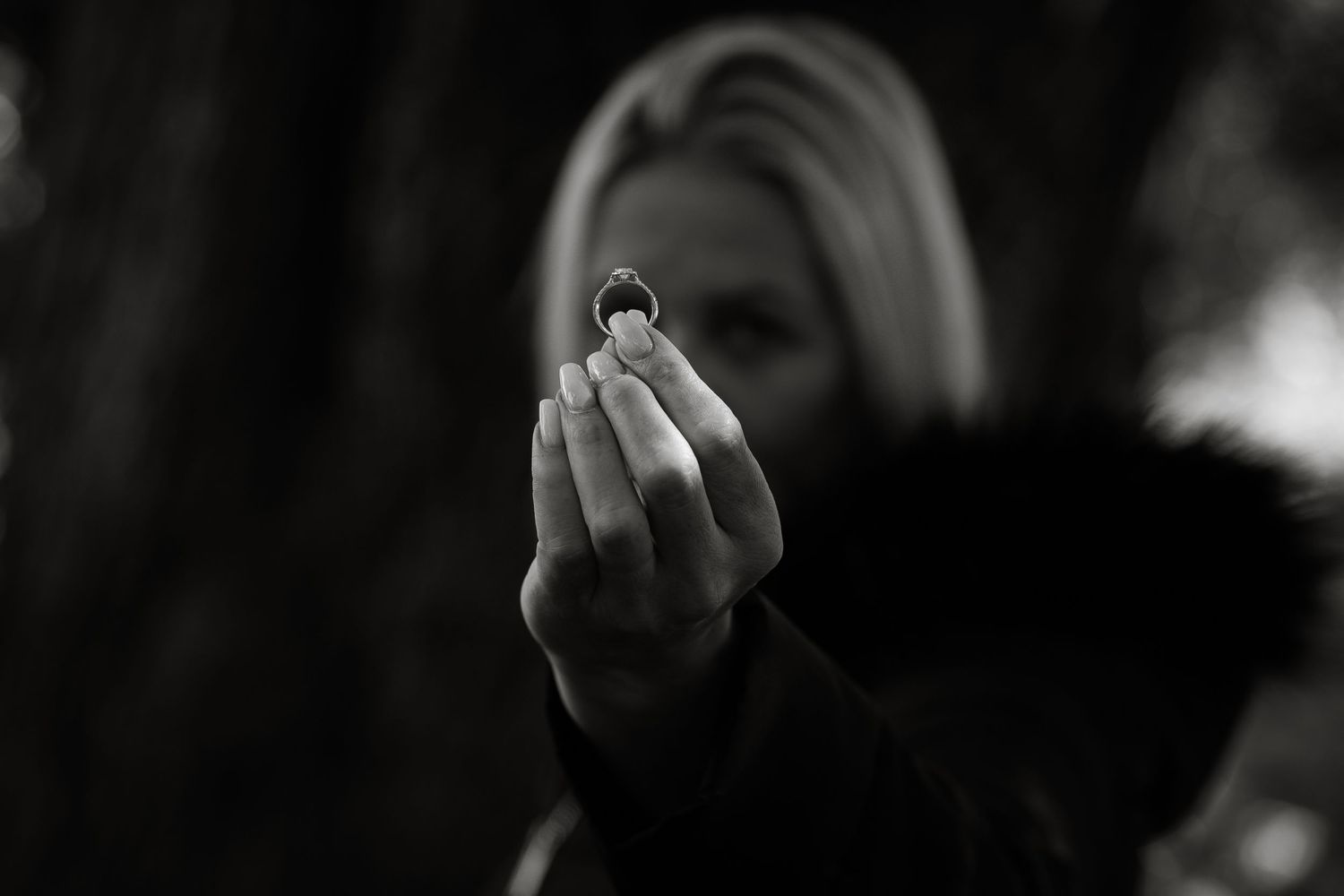 A close-up black and white photo of hands holding an engagement ring.