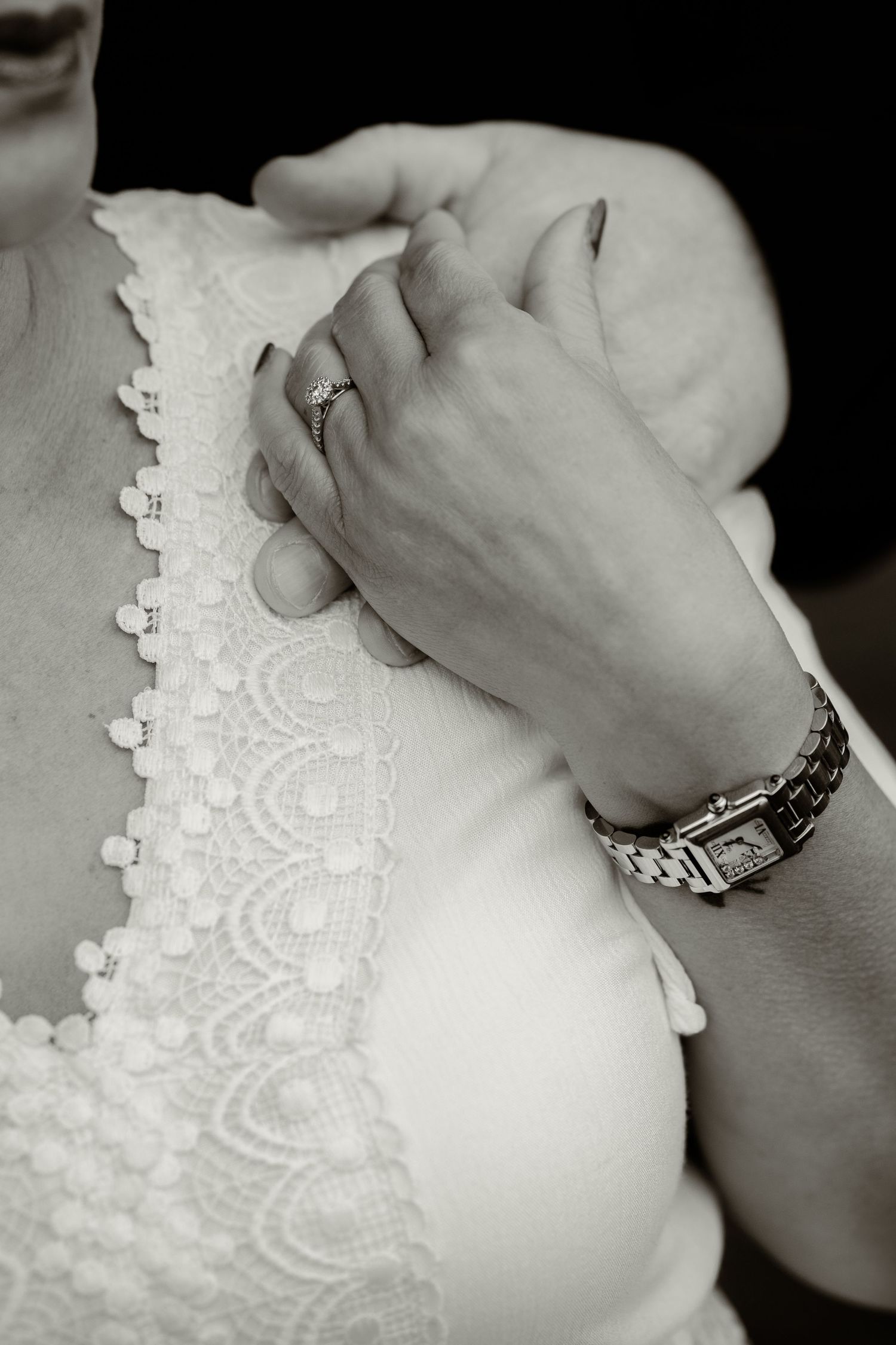 Close-up black and white photo of a wedding dress detail and hands showing jewelry.
