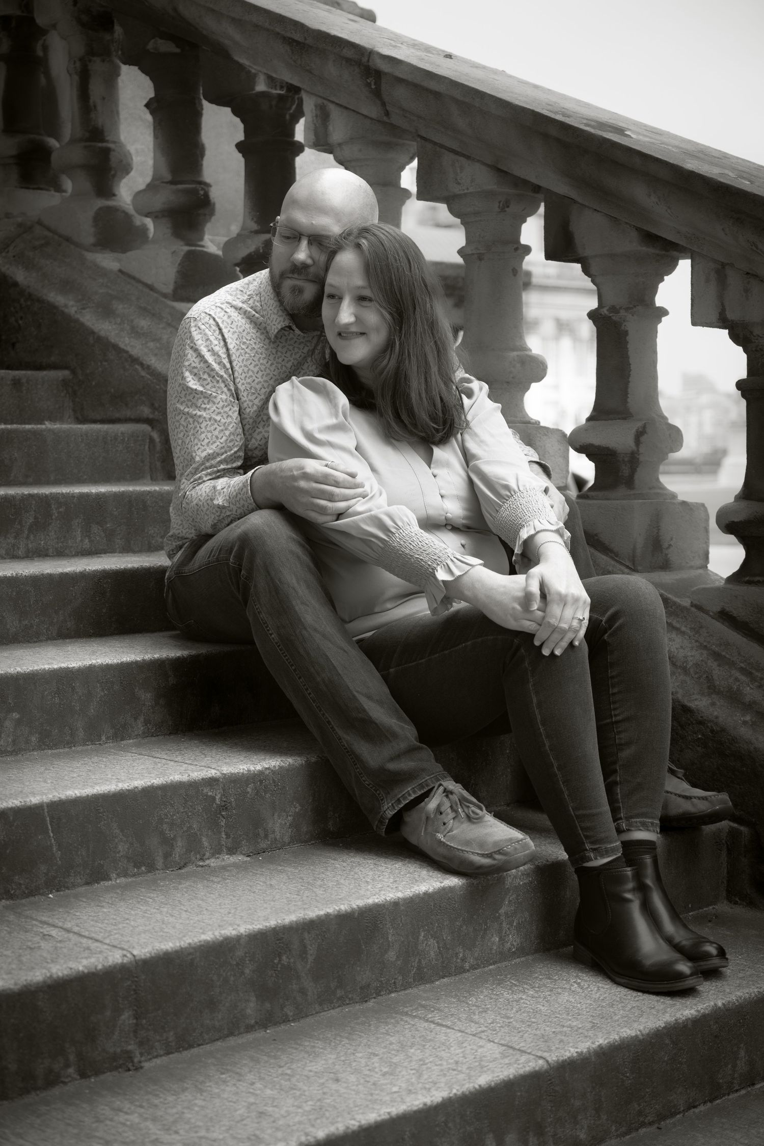 A black and white portrait of a couple sitting intimately on stone steps.