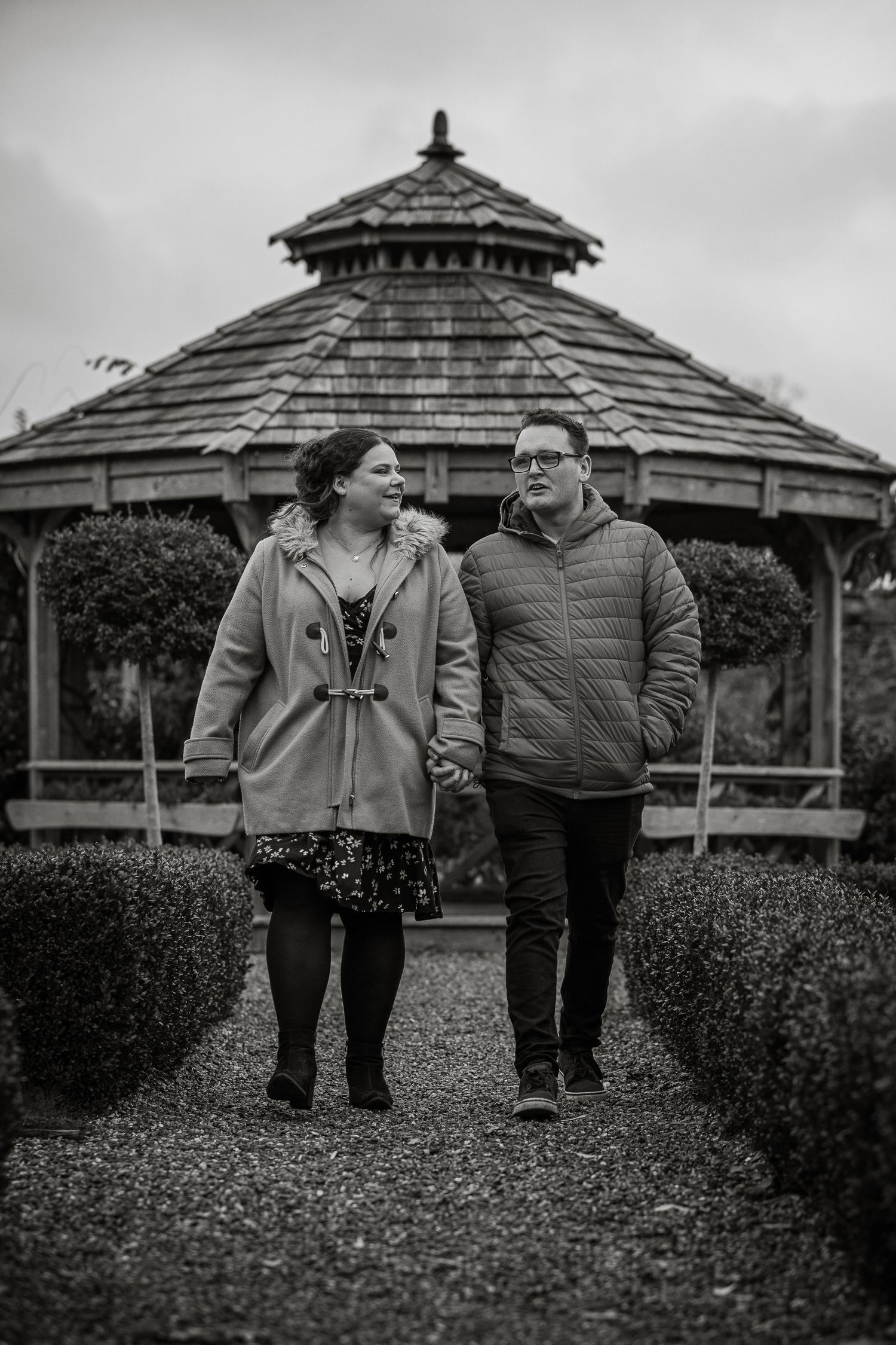A black and white photo series of a couple walking together near a gazebo in a park.