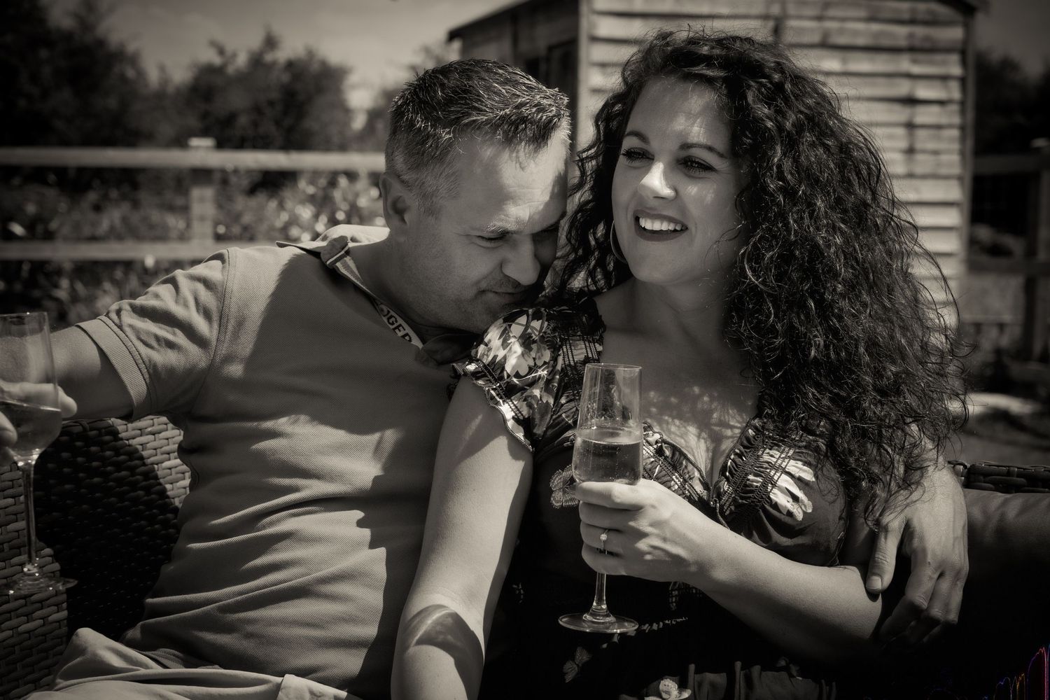A romantic couple sharing a laugh while holding wine glasses outdoors.