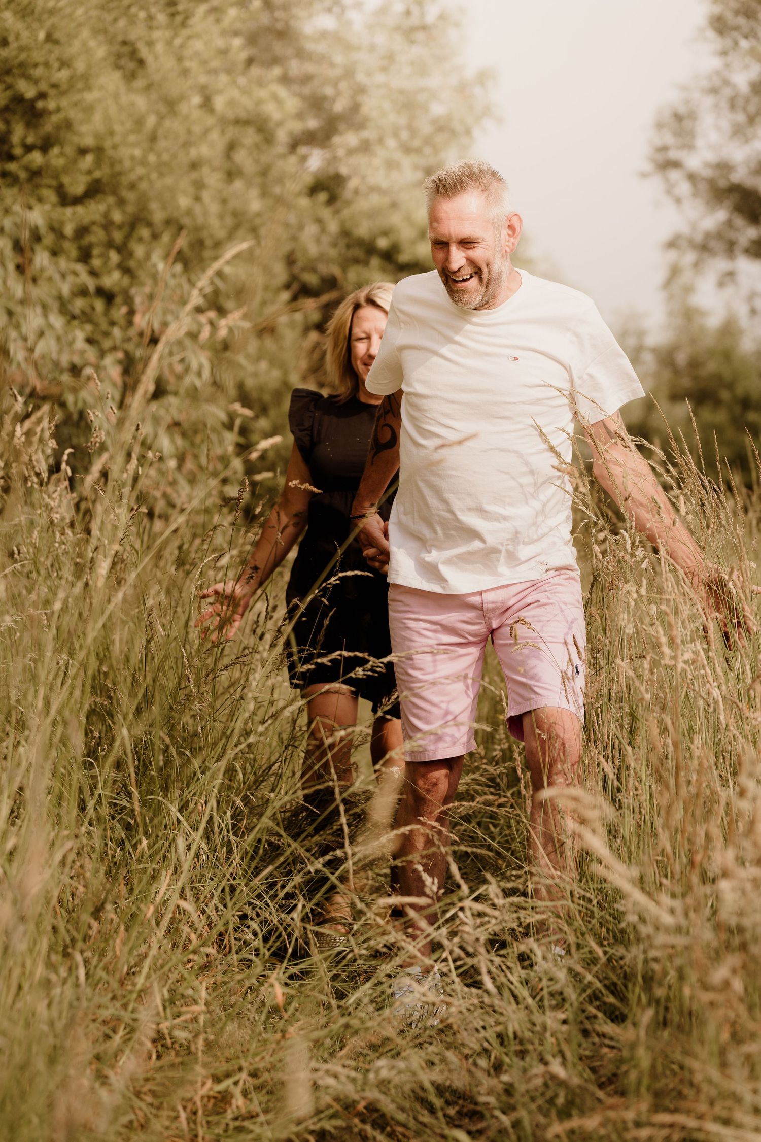 A joyful couple walking through tall meadow grass during golden hour.