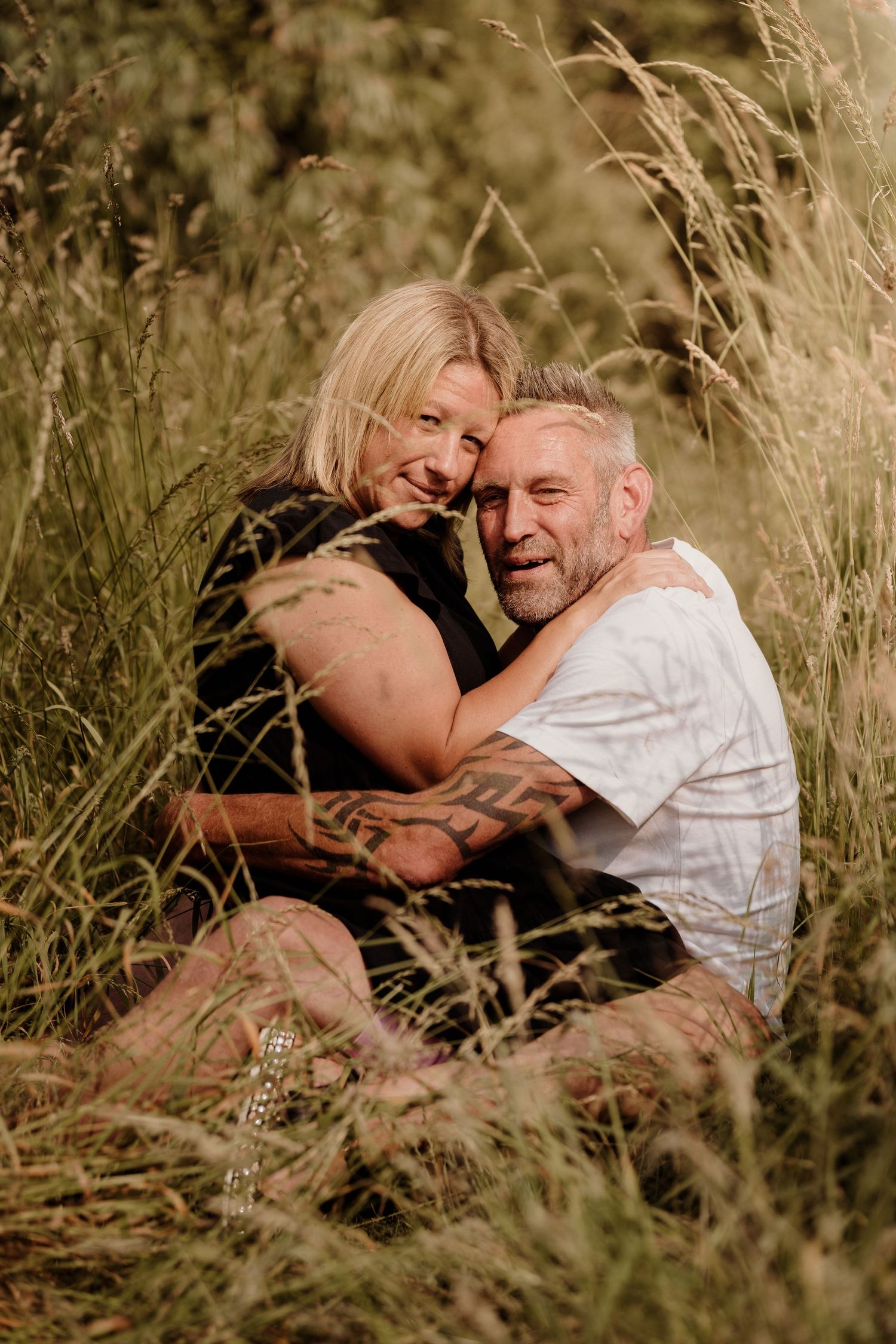 A candid portrait of a couple laughing together while sitting in tall golden grass.