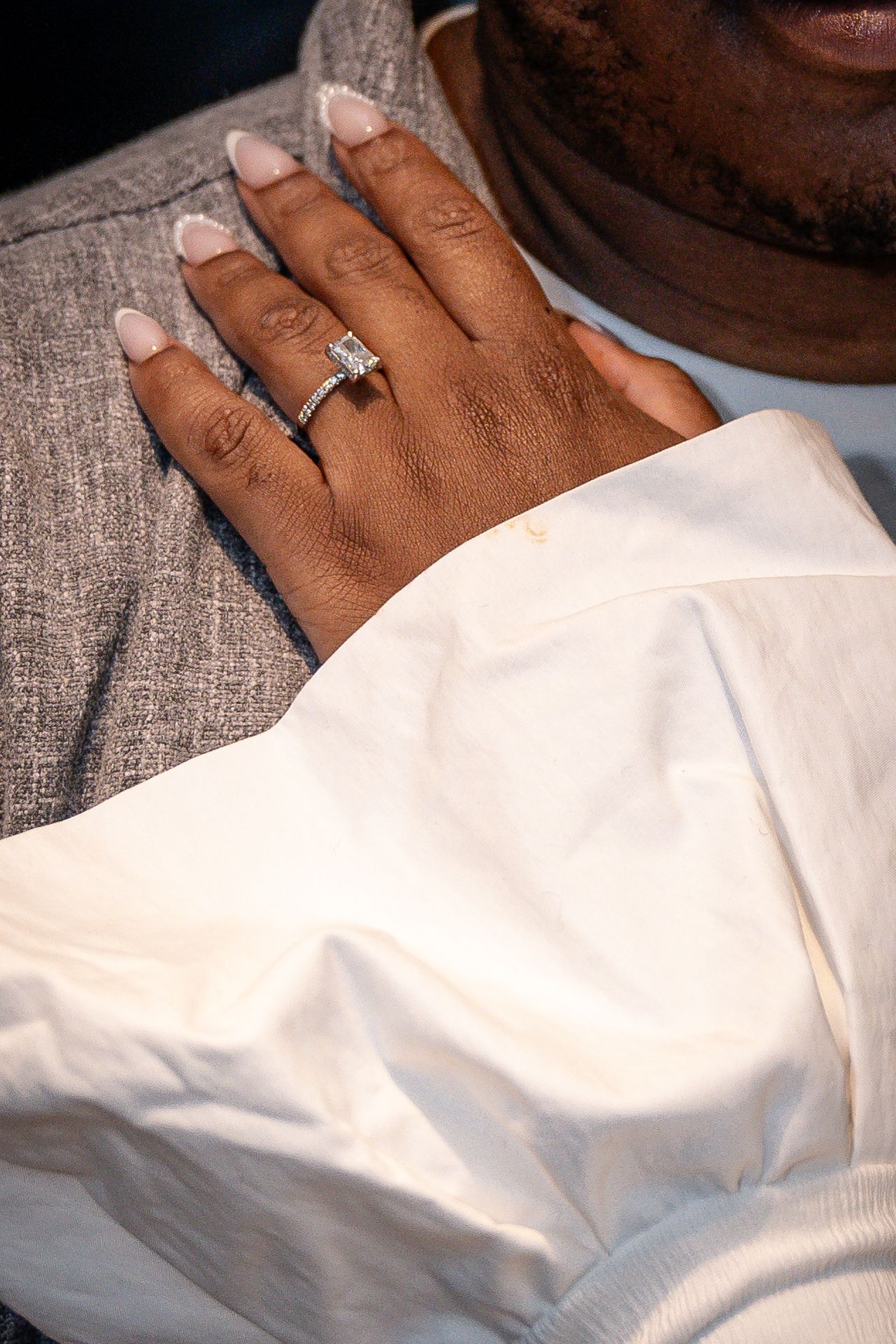 Close-up of a hand wearing a sparkling diamond engagement ring against a white fabric background.