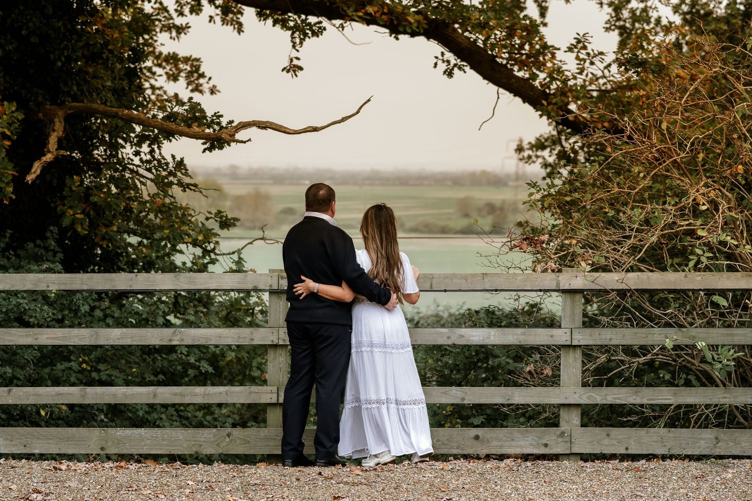 A couple stands embracing at a scenic overlook with a natural landscape view in the background.